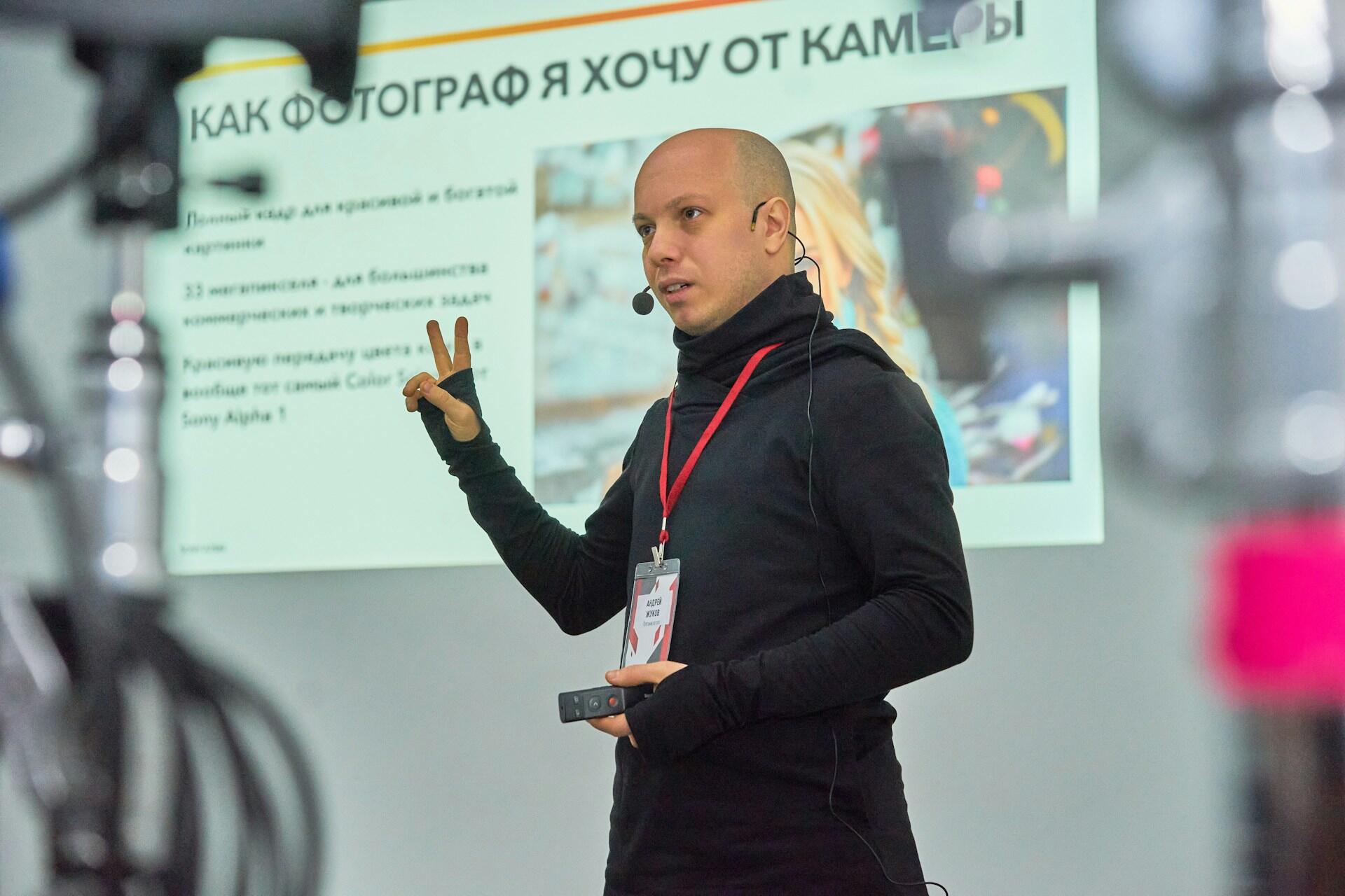 A man wearing black stands in front of a slideshow presentation.