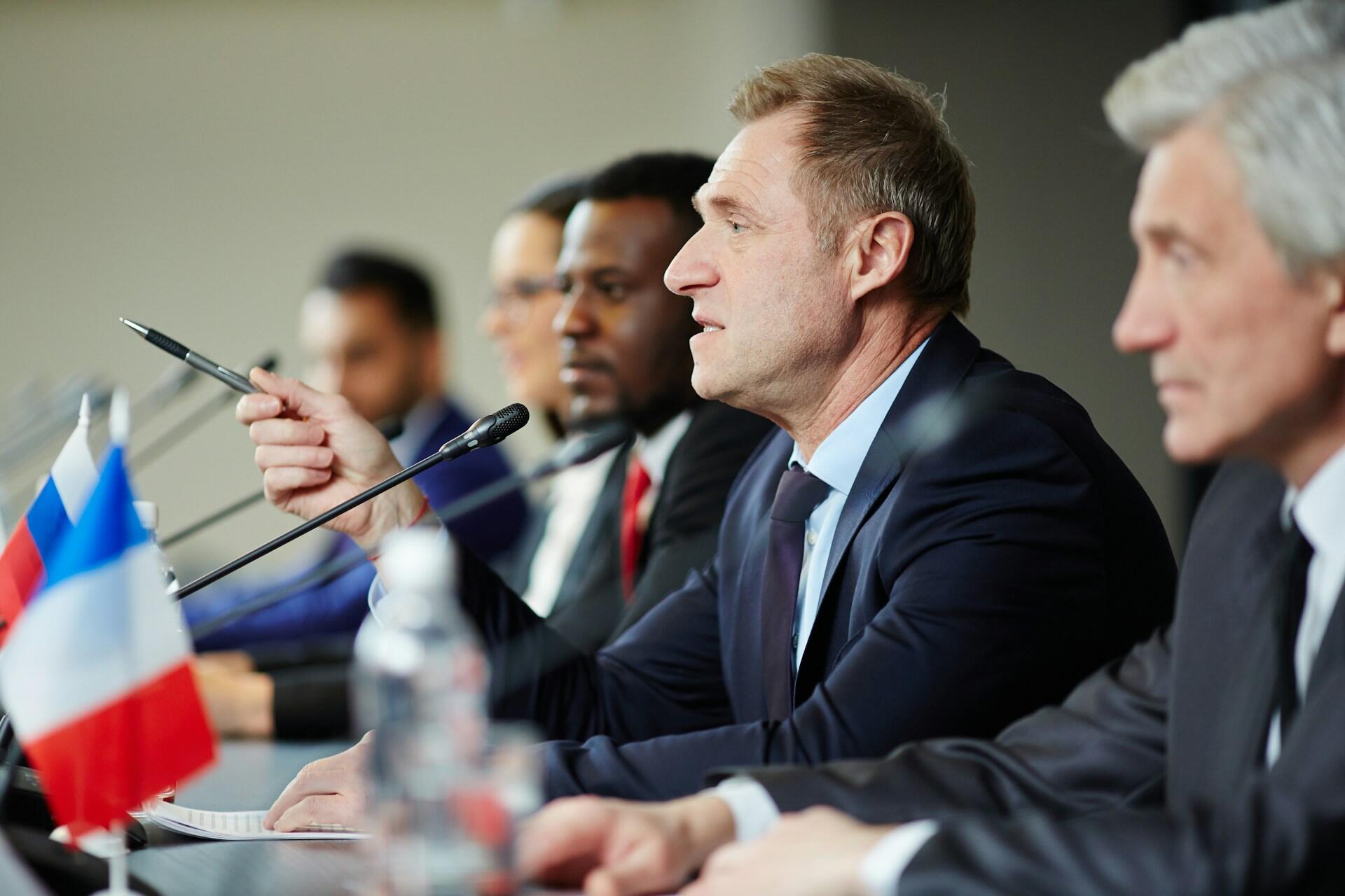 Men in suits sittinng at a table decorated with flags.