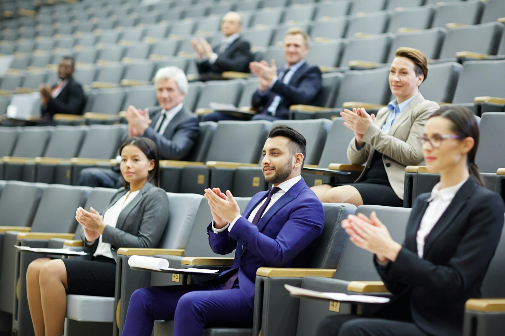 People in business attire clapping in an auditorium.