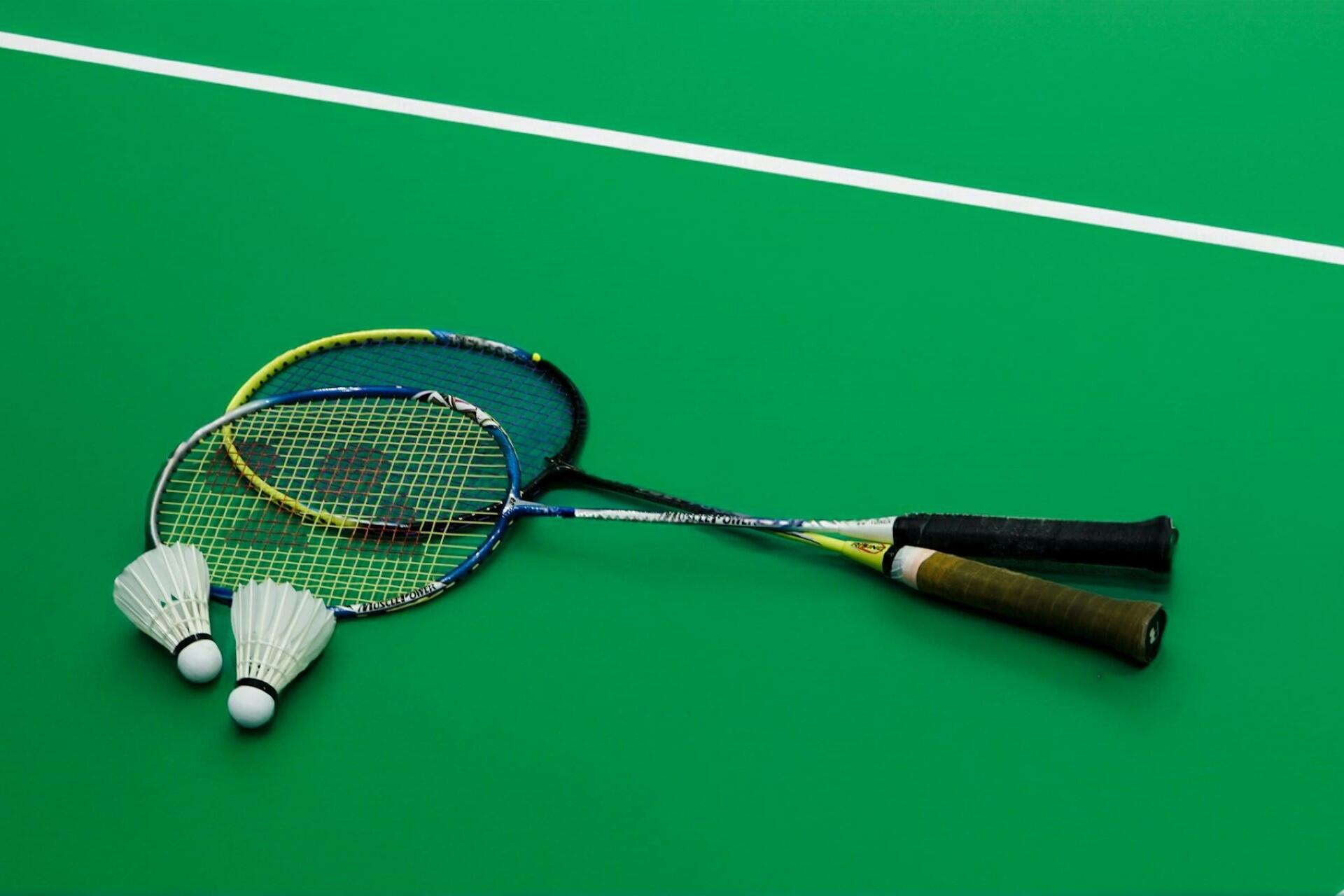 A couple of badminton racquets next to shuttlecocks on a court.