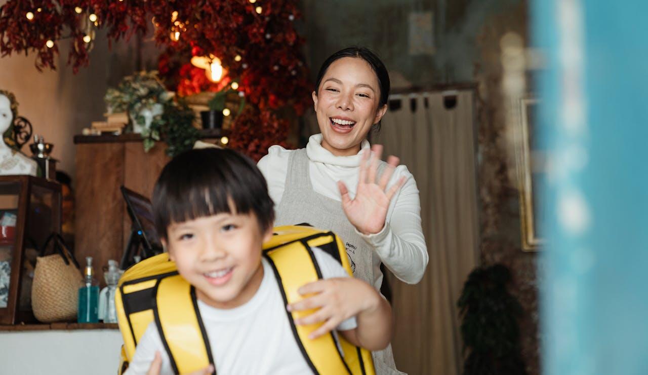 A woman gestures with a hand raised while assisting a child wearing a yellow flotation device in a cozy, decorated indoor space.