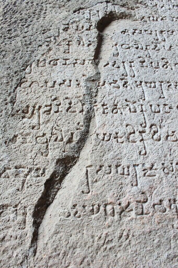 Ancient stone tablet with engraved script, featuring visible cracks running through the inscriptions.
