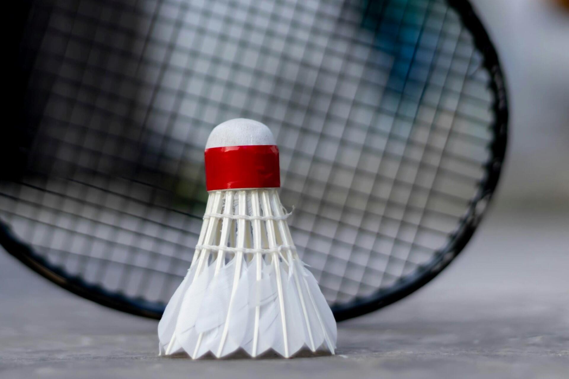 A shuttlecock on the ground next to a badminton racquet.