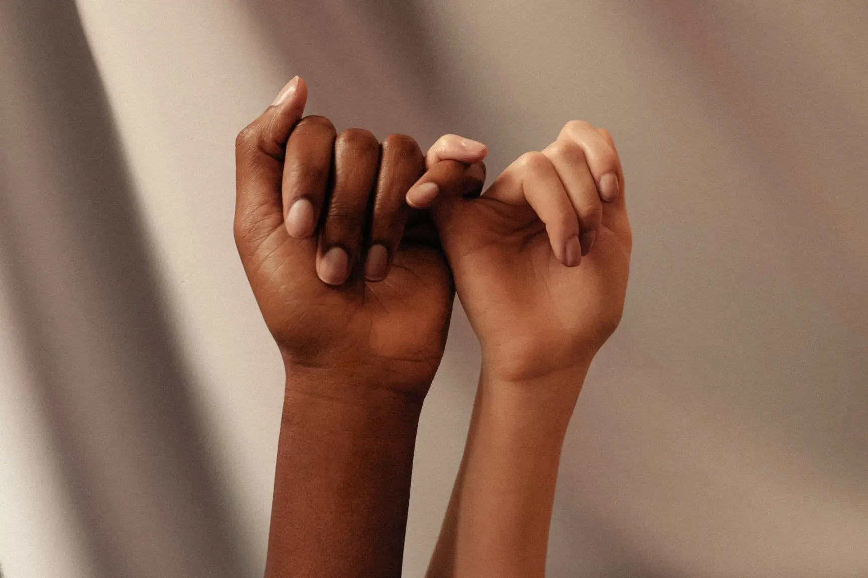 two people crossing pinky fingers with hands held upwards