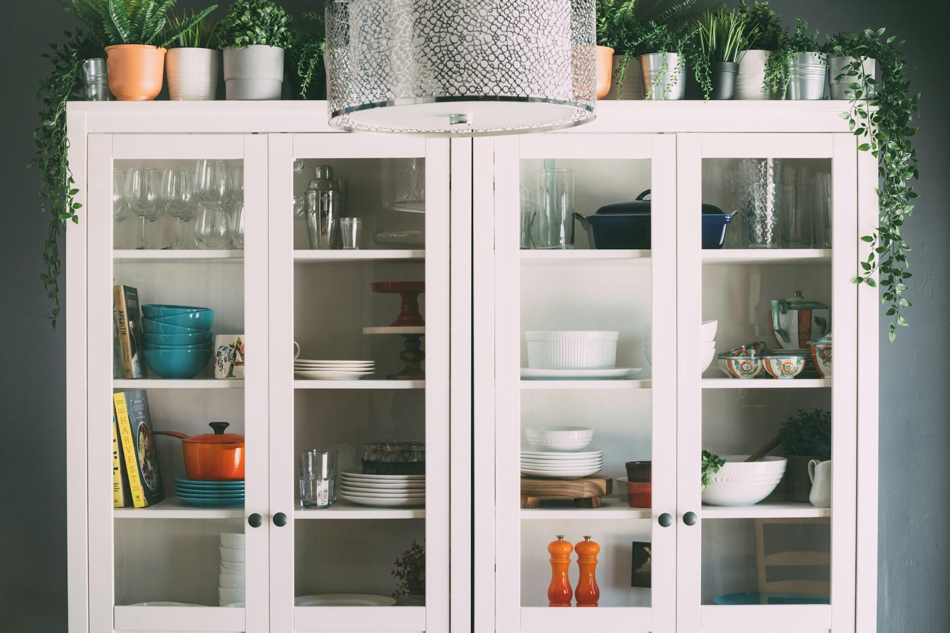 A while cupboard with dishes inside it and stacked on it.
