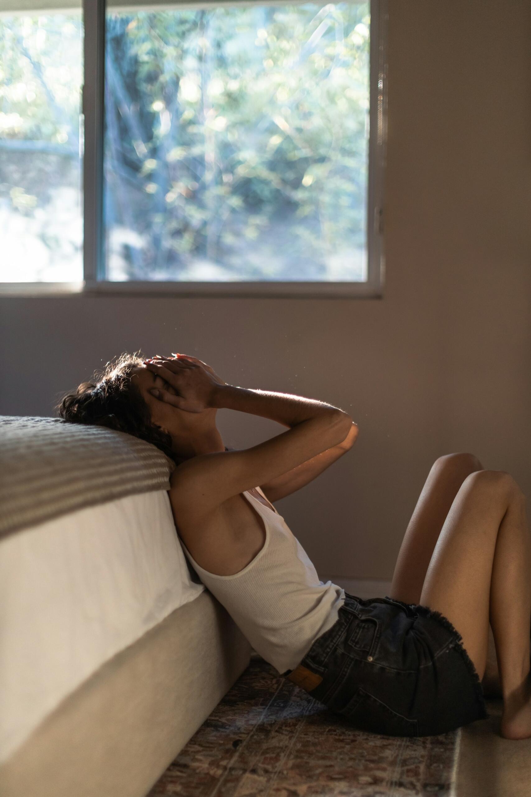 A person sitting on the floor with their hands over their face.