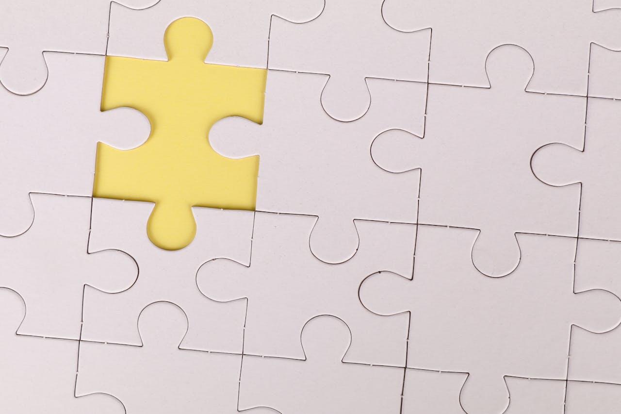A single yellow puzzle piece is positioned above an empty space on a white, scattered puzzle board.