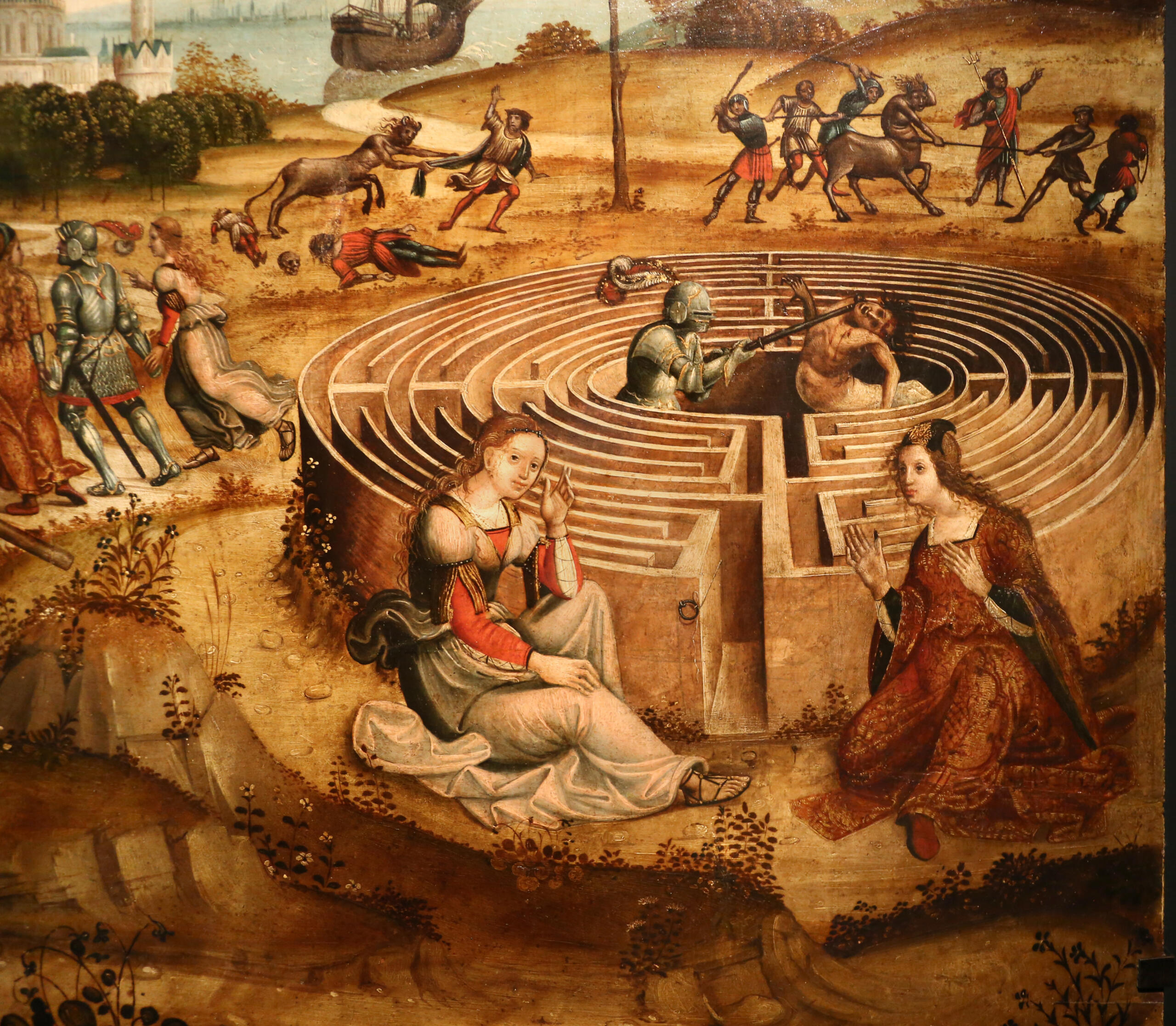 Medieval painting of a labyrinth scene. Two women sit outside; knights enter, and one fights a Minotaur inside. In the background are more figures and landscape. The tone is mystical and adventurous.