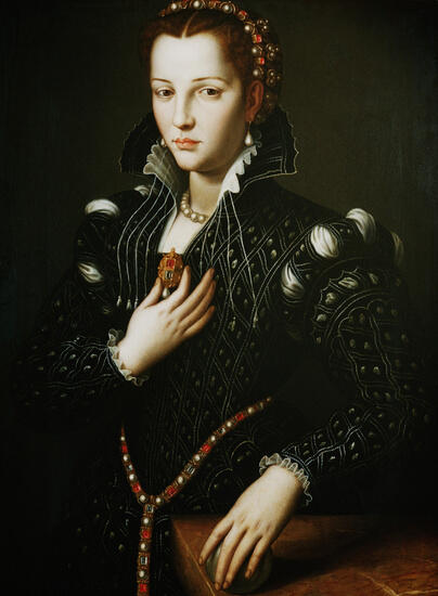 A woman in a richly detailed black gown adorned with jewels, presenting an elegant pose against a dark background.