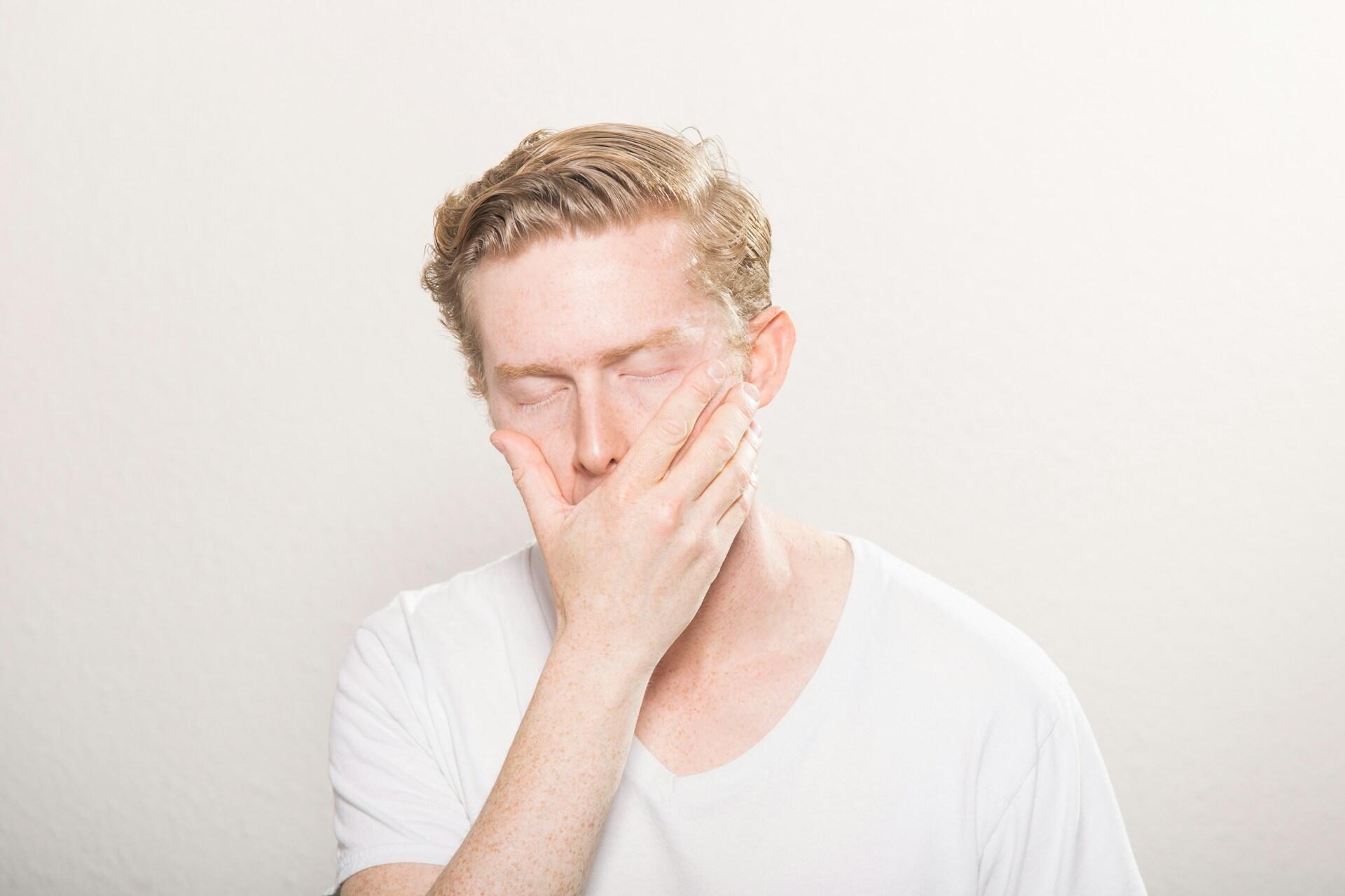A man in a white shirt with his hand over his mouth.