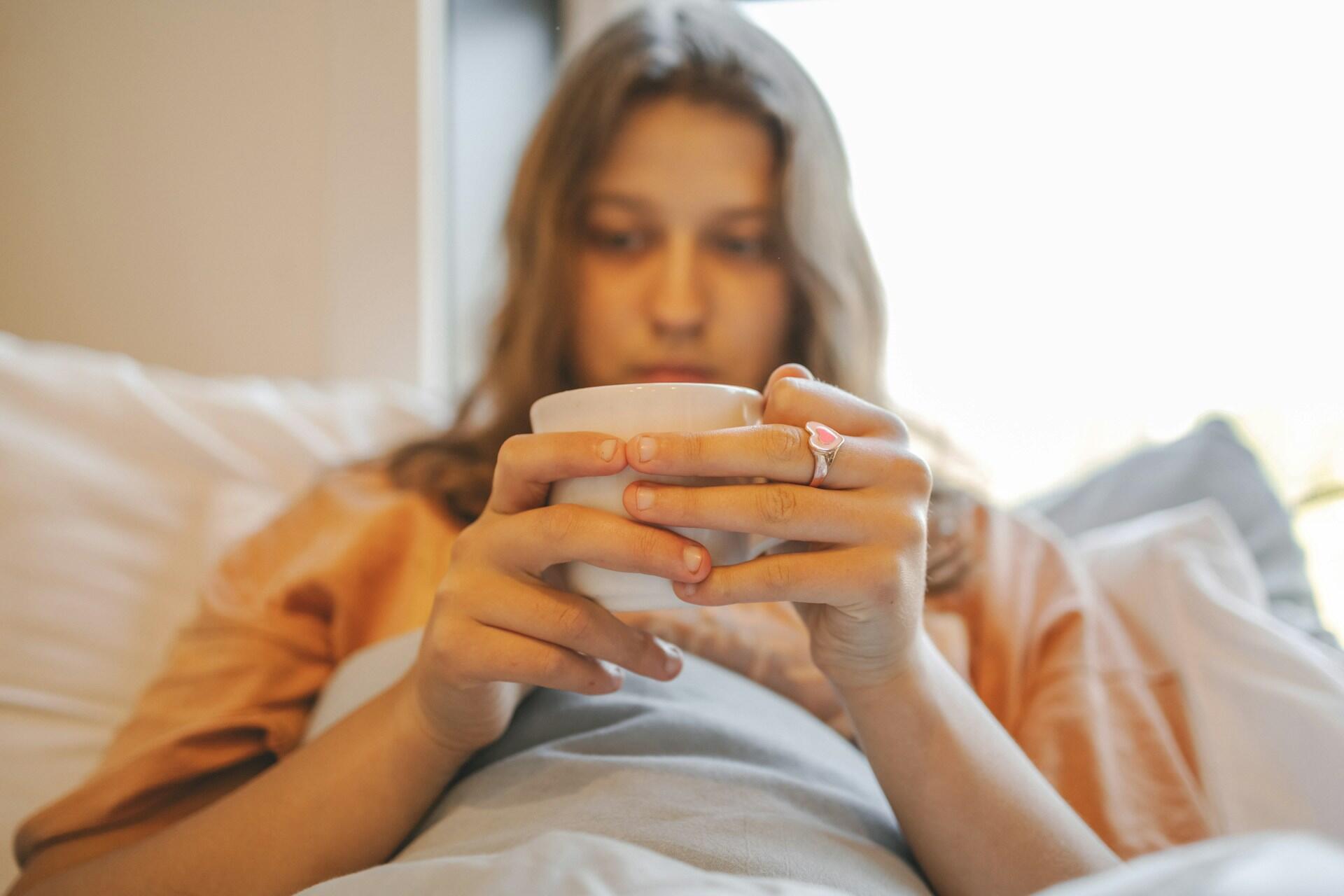 A woman in bed holding a cup.