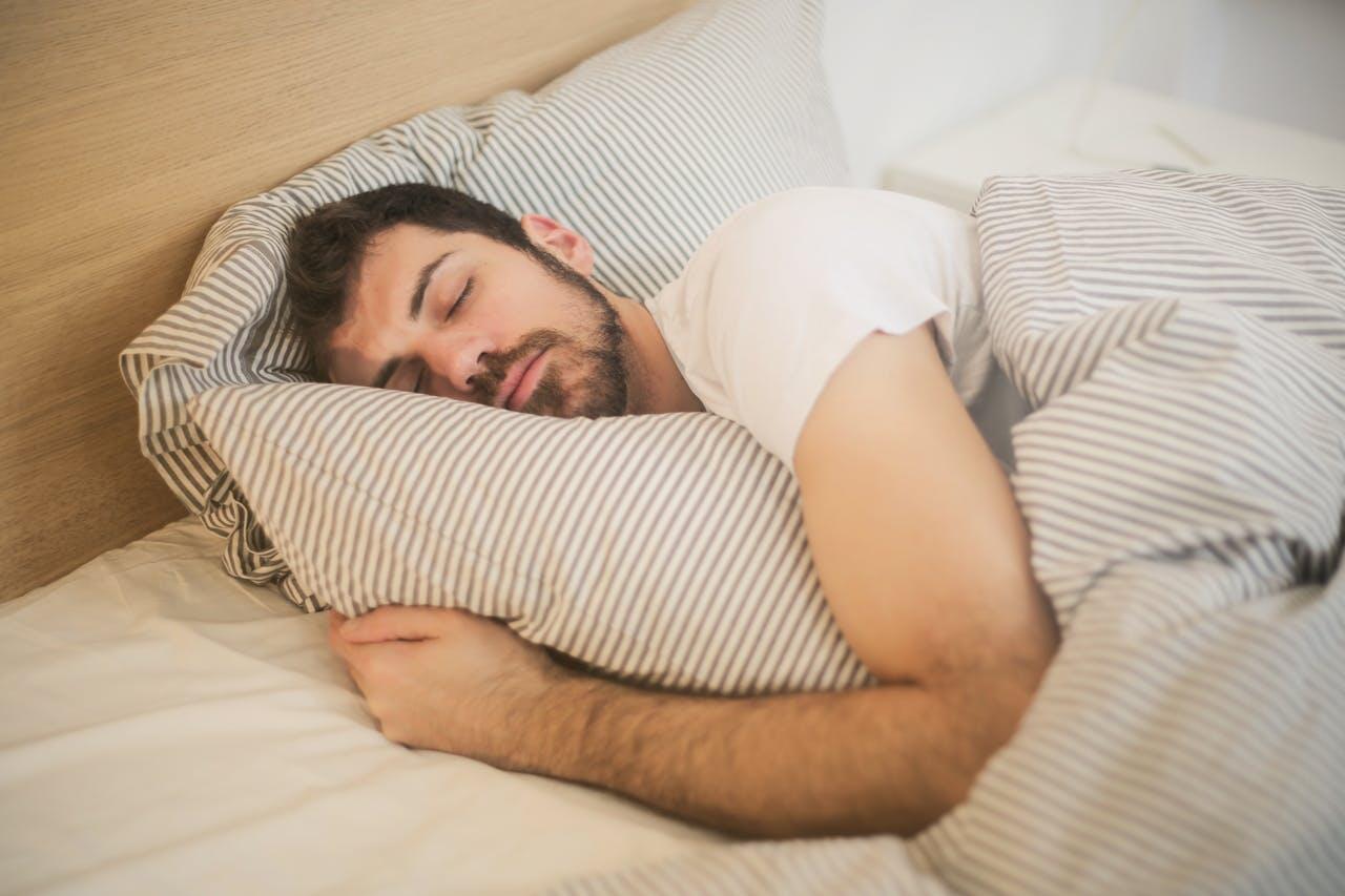 A person curled up in bed, comfortably resting on striped pillows, surrounded by cozy bedding.