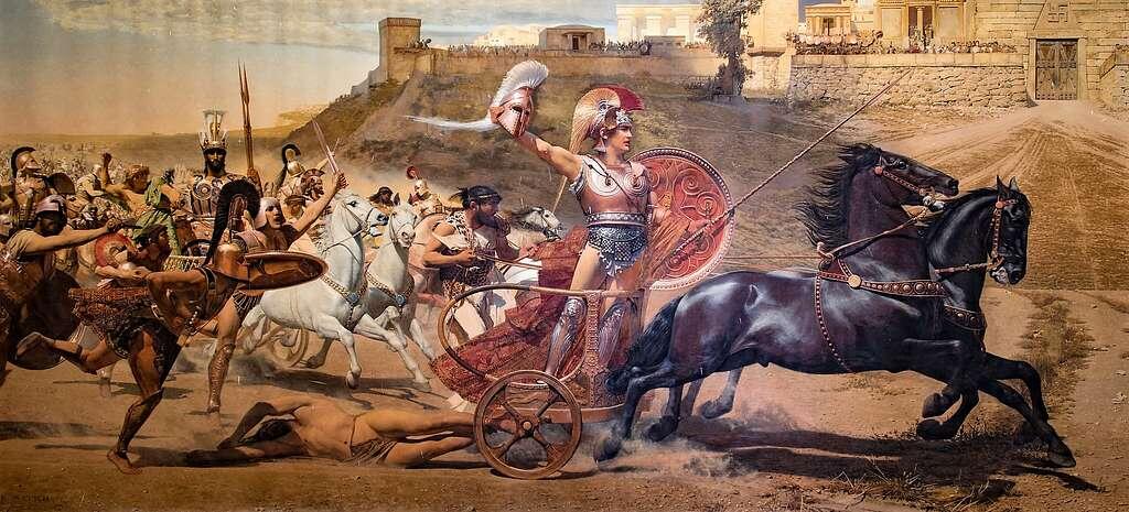 A warrior in ornate armor and helmet stands on a chariot pulled by two horses, dragging a fallen soldier. Ancient city walls loom in the background. Intense action.