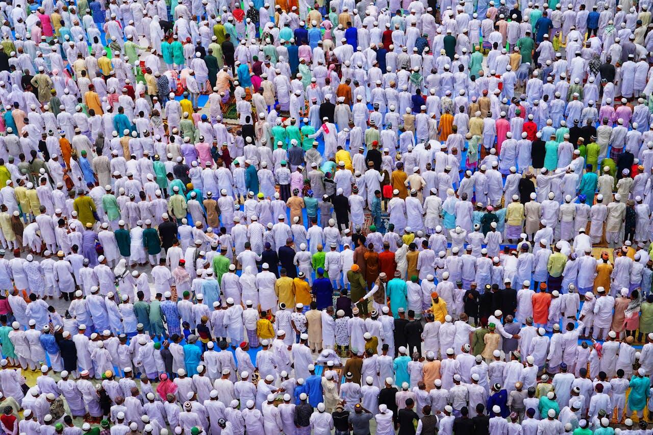 Aerial view of a diverse crowd of people dressed in traditional white garments, gathered for a religious event or prayer.