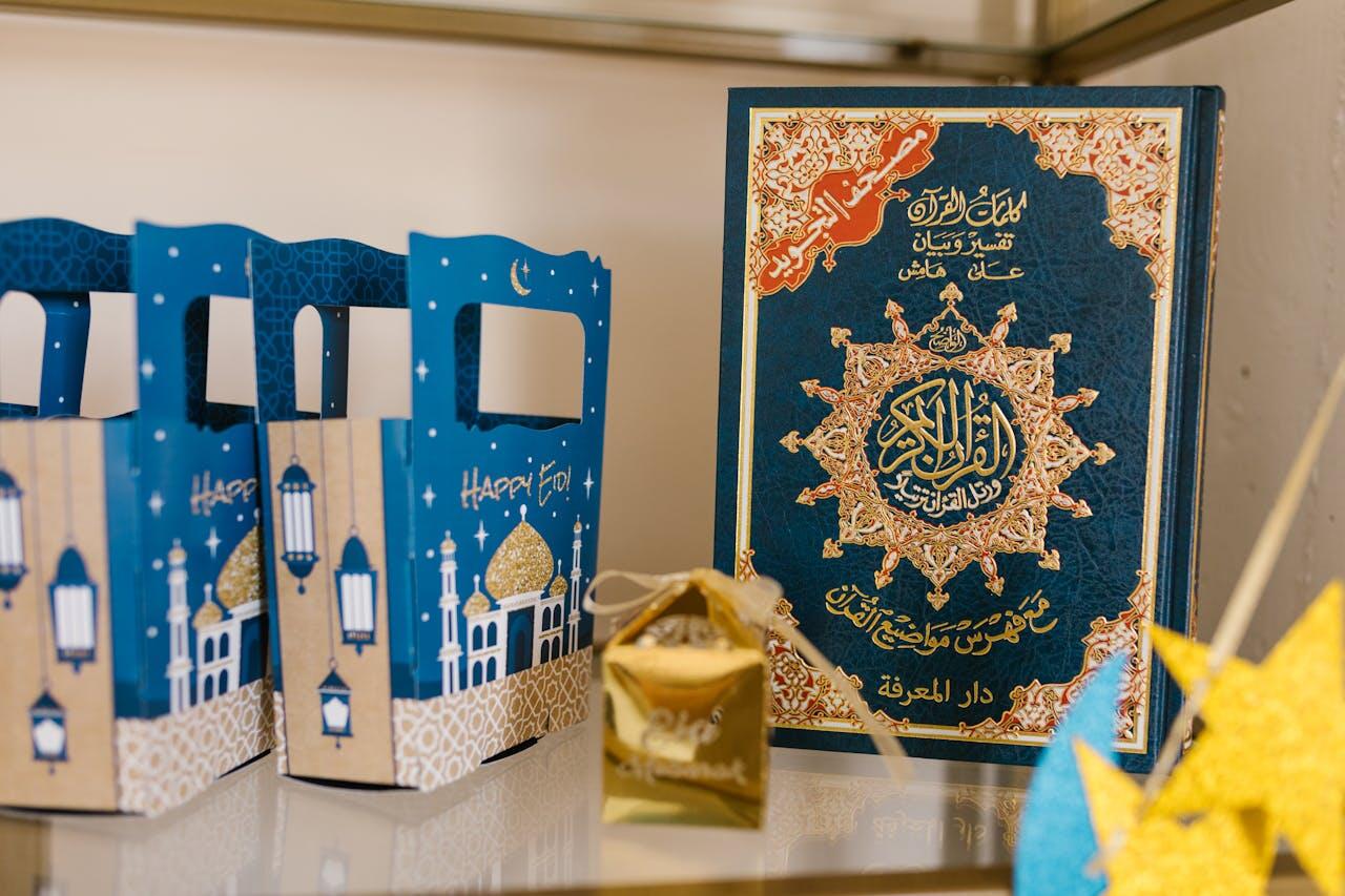 A decorative blue gift bag and a gold-wrapped treat beside a beautifully ornate Quran on a shelf, celebrating Eid.