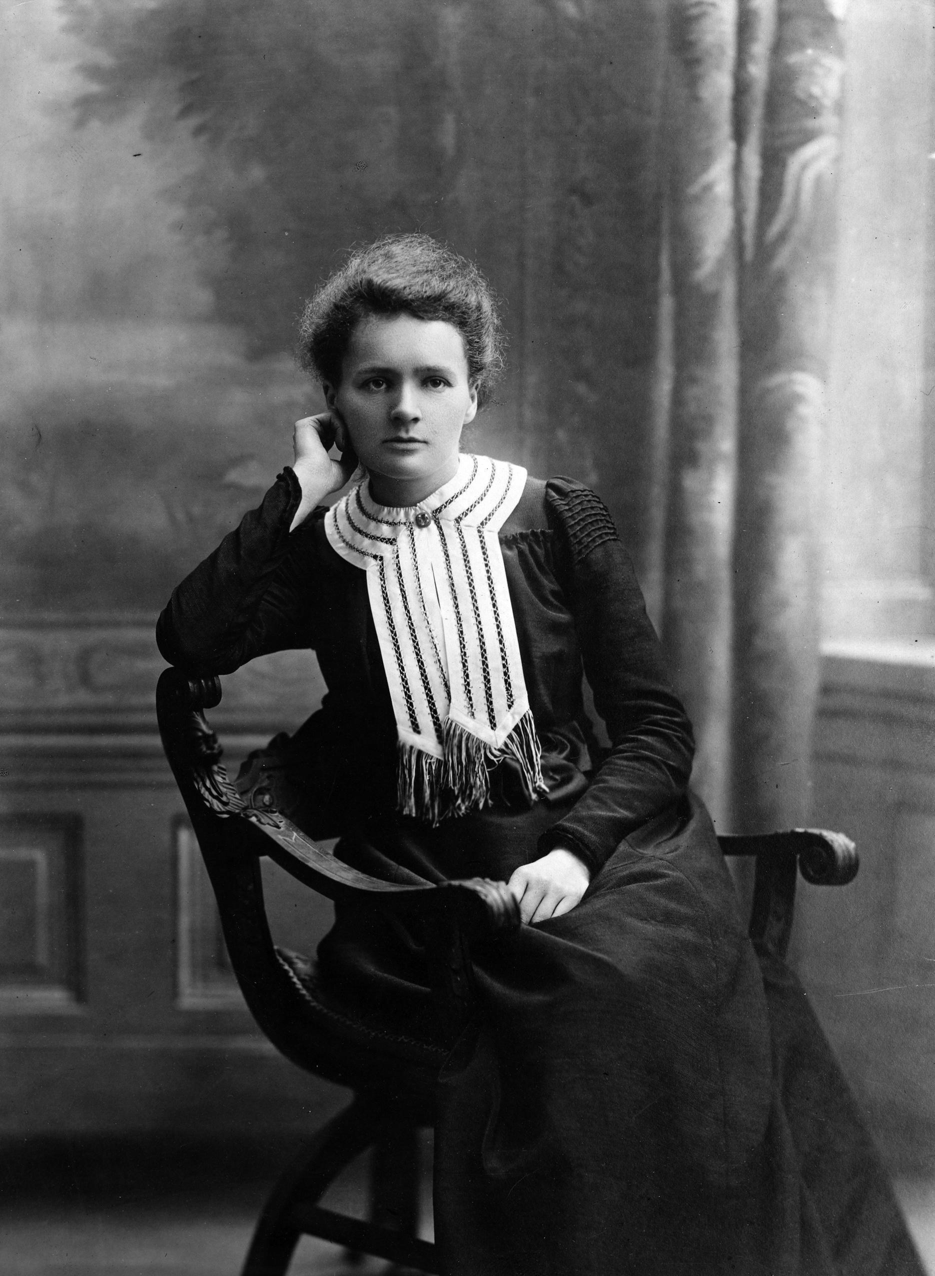 Black and white photo of Marie Curie sitting on a chair.