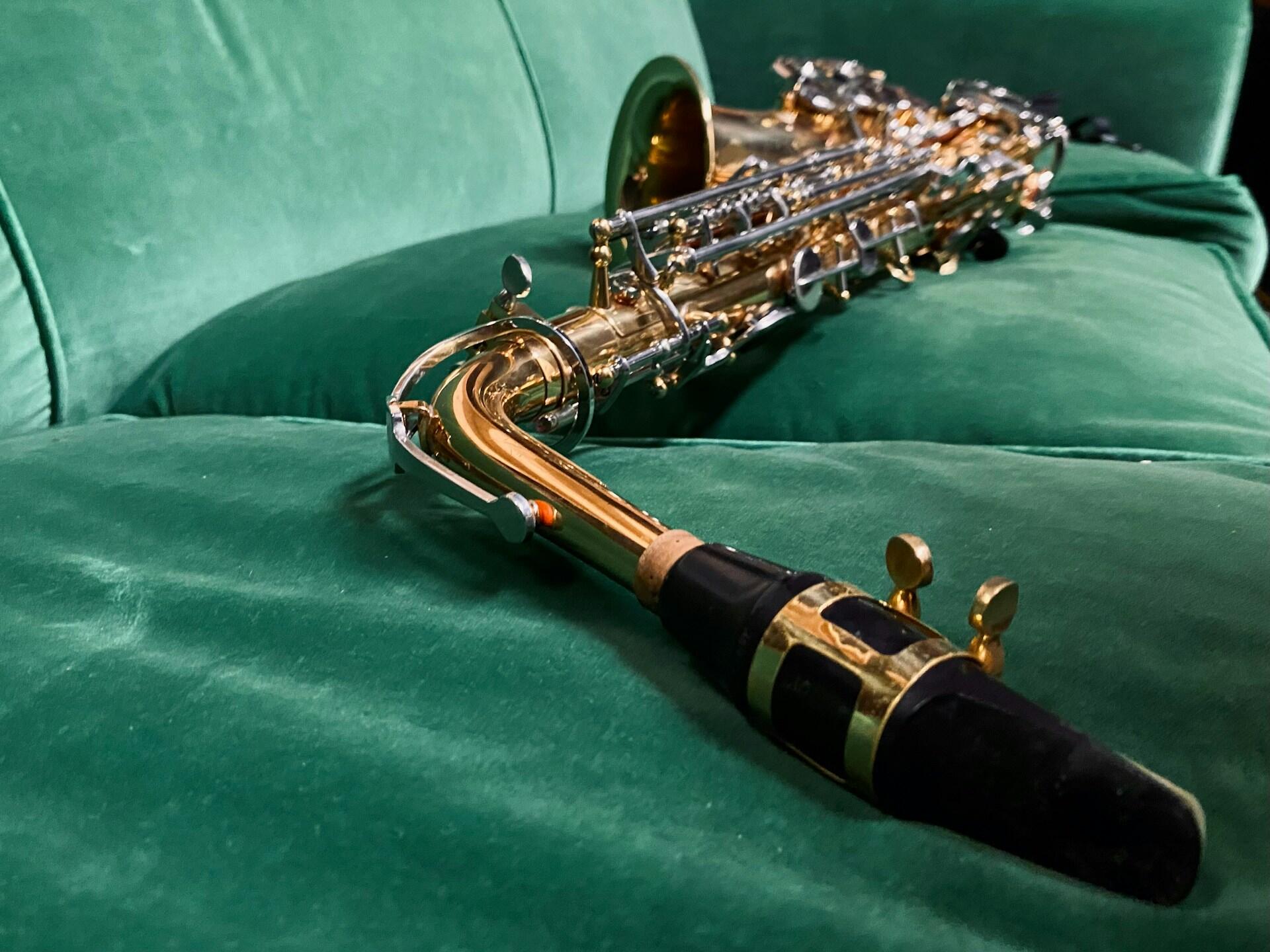 A closeup of a saxophone mouthpiece on a green couch.