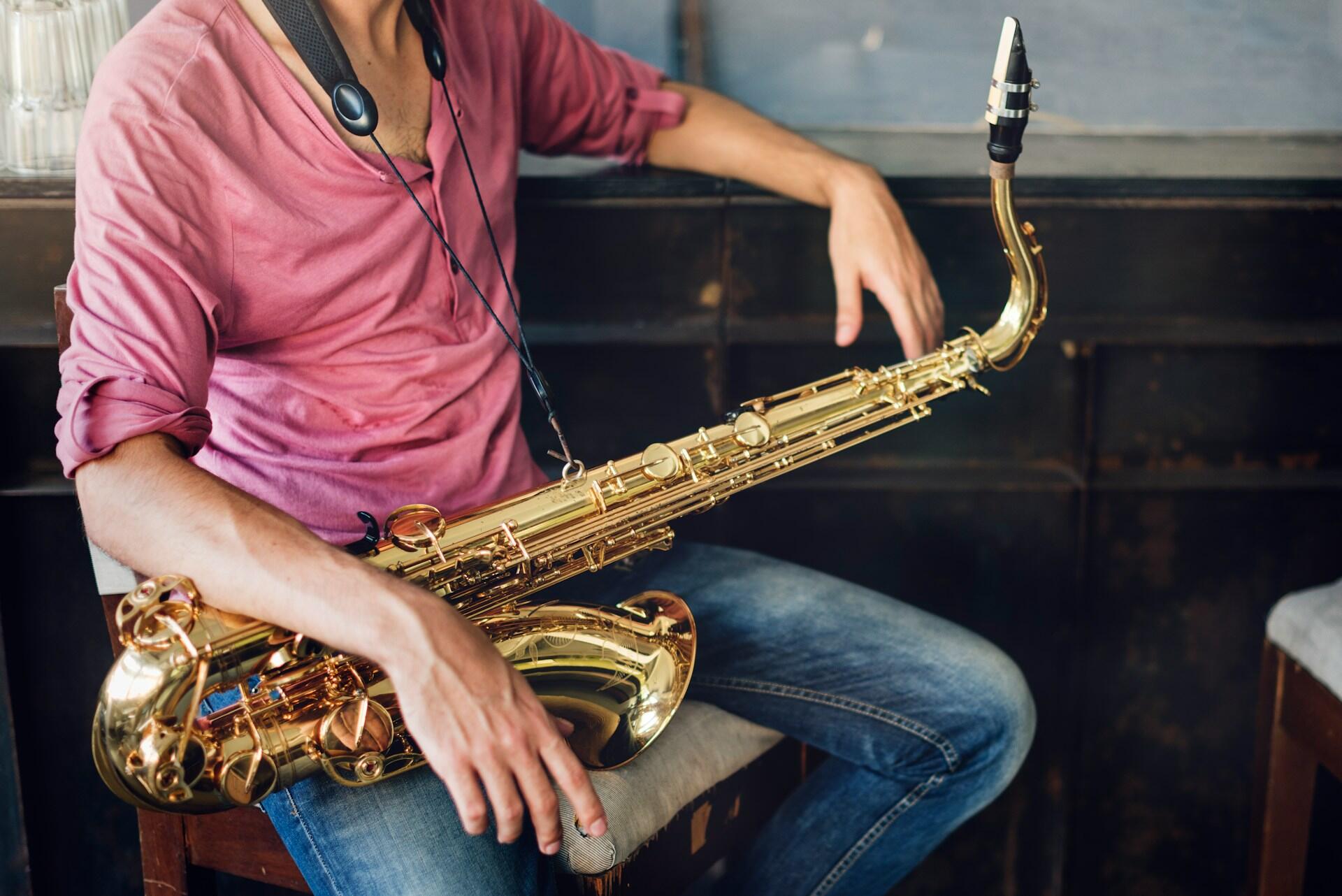 A man in a pink shirt sits with his arm slung over a saxophone