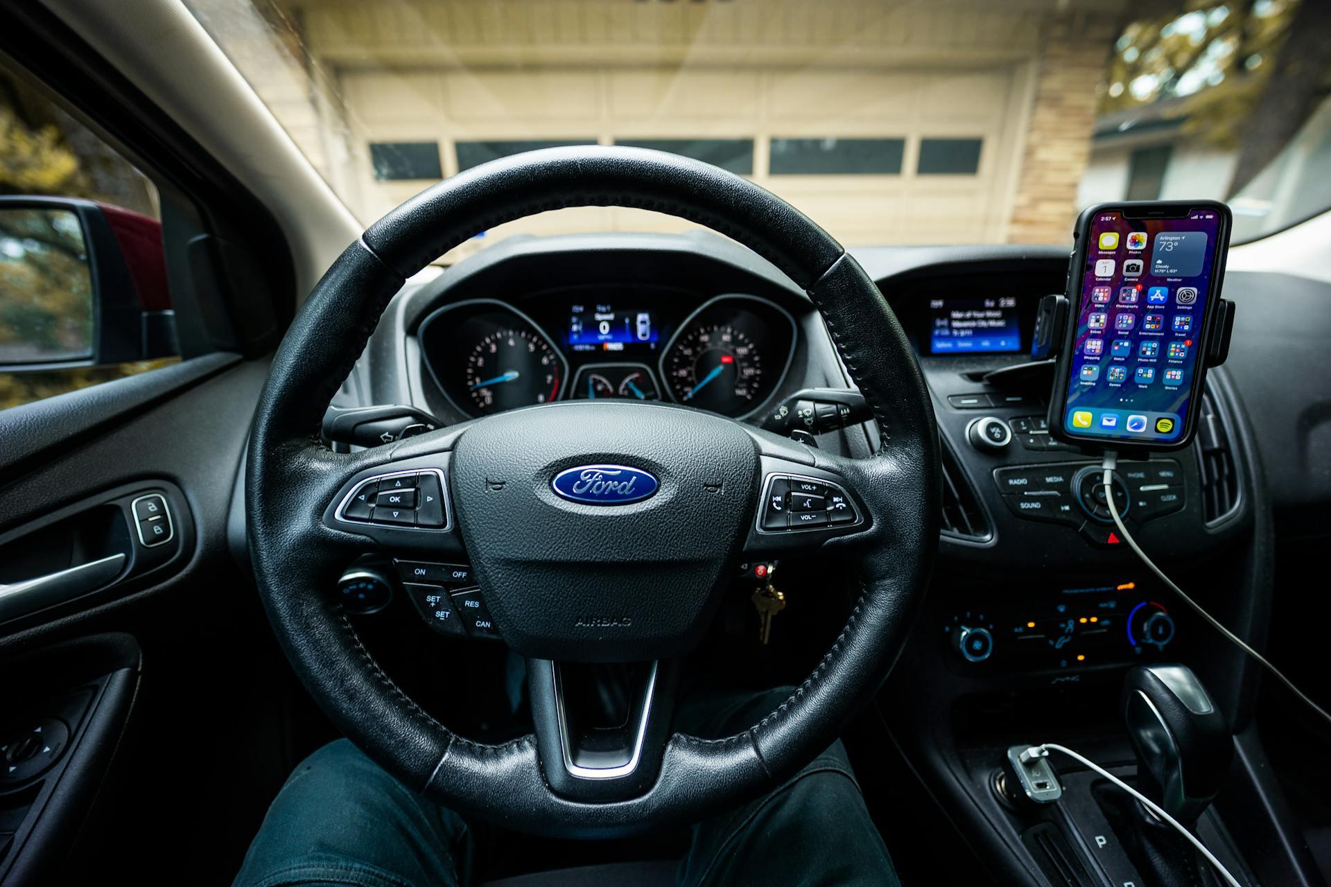The inside of a Ford vehicle featuring an iPhone and the steering wheel.