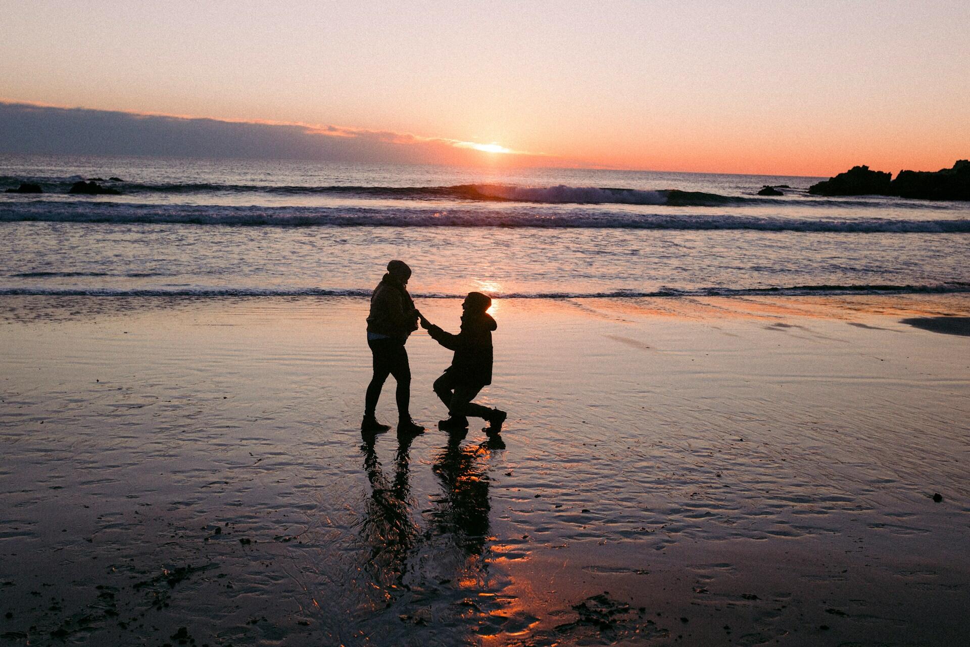 person proposing to their partner on a beach at sunset