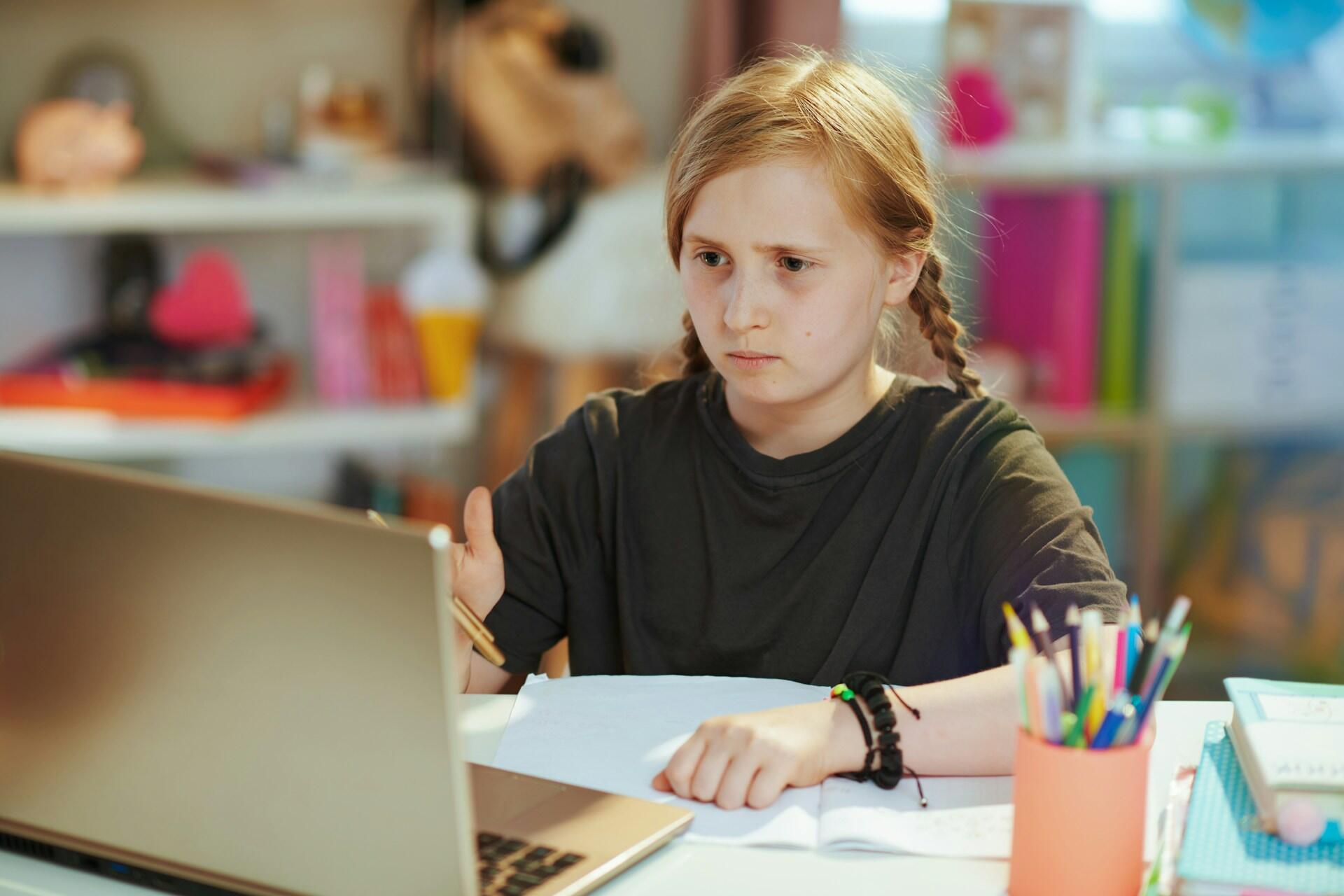 A student sits in front of a computer with a frown on their face.