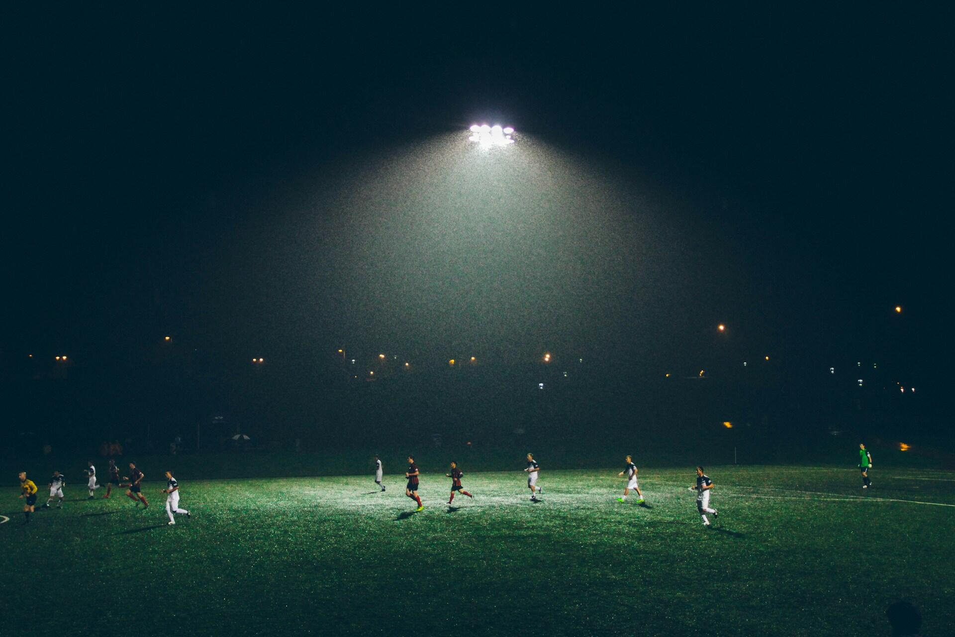 Football match being played at night under floodlights