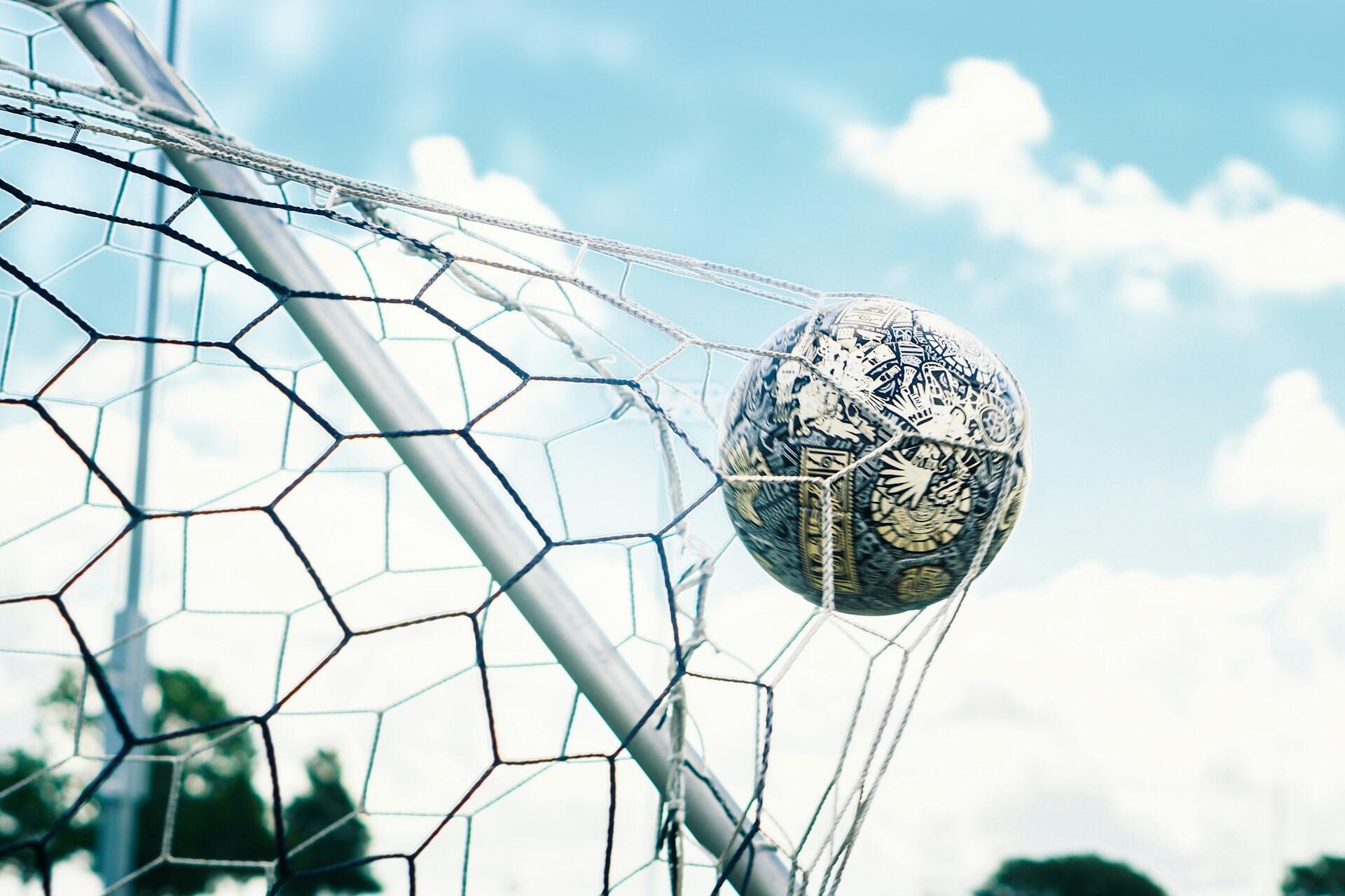 Football caught in a goal net against a bright blue sky