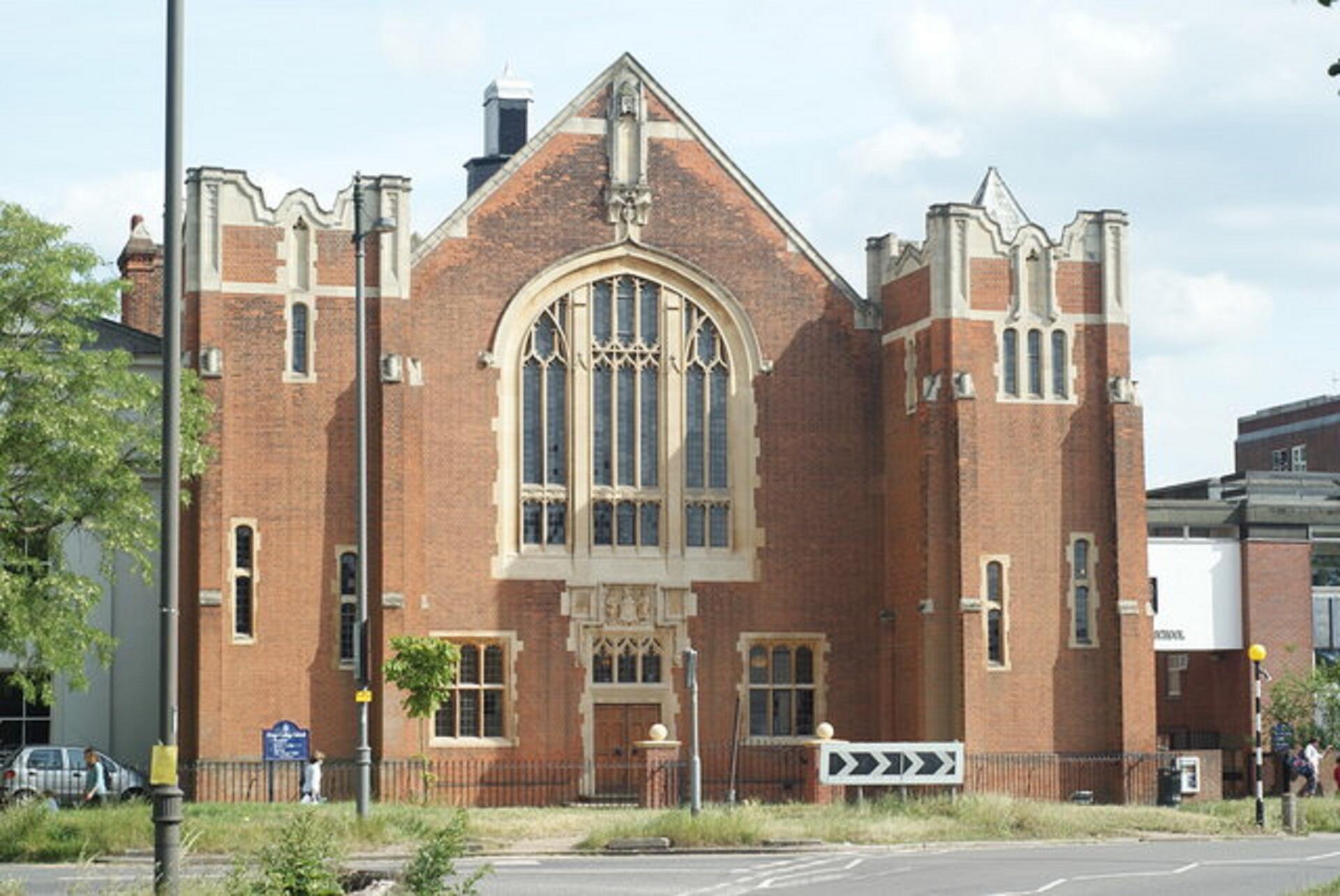 A large red brick building with a large arched window and two flanking towers.