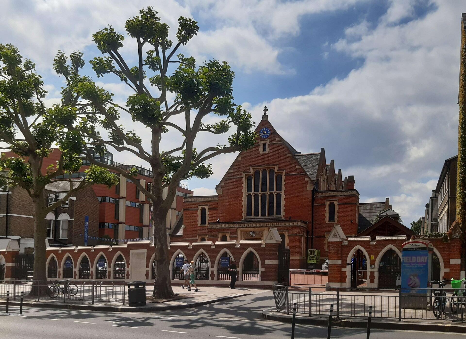 A large brick building with distinctive roof lines behind a low, arched wall.