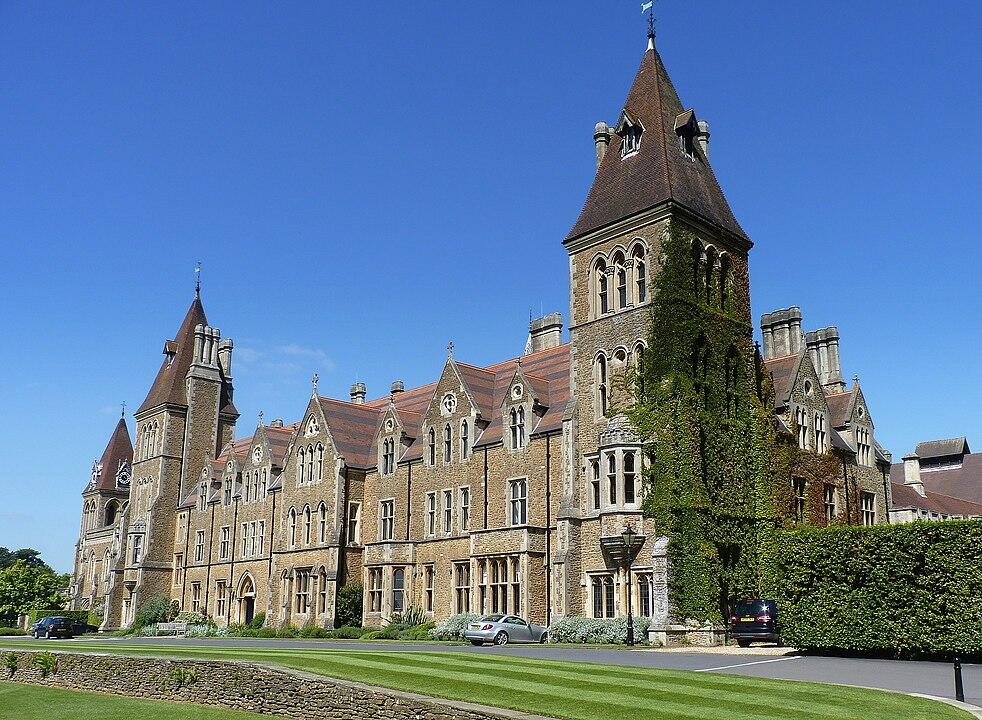 Victorian-style building with towers and ivy, set against a clear blue sky, surrounded by lush green lawns.