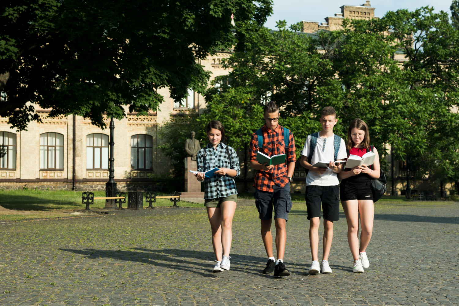 A group of five young athletes in sports uniforms stand closely together, smiling and enjoying a sunny day outdoors.