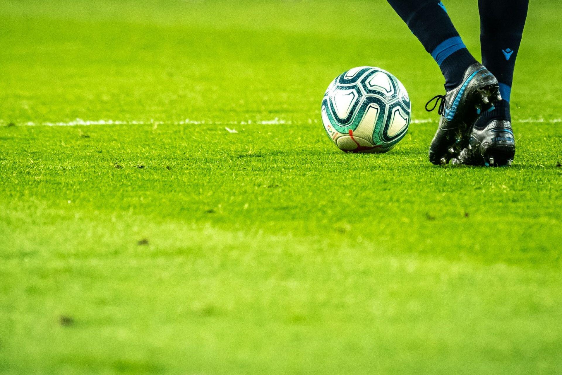 Football beside a player's black boots on a grass pitch