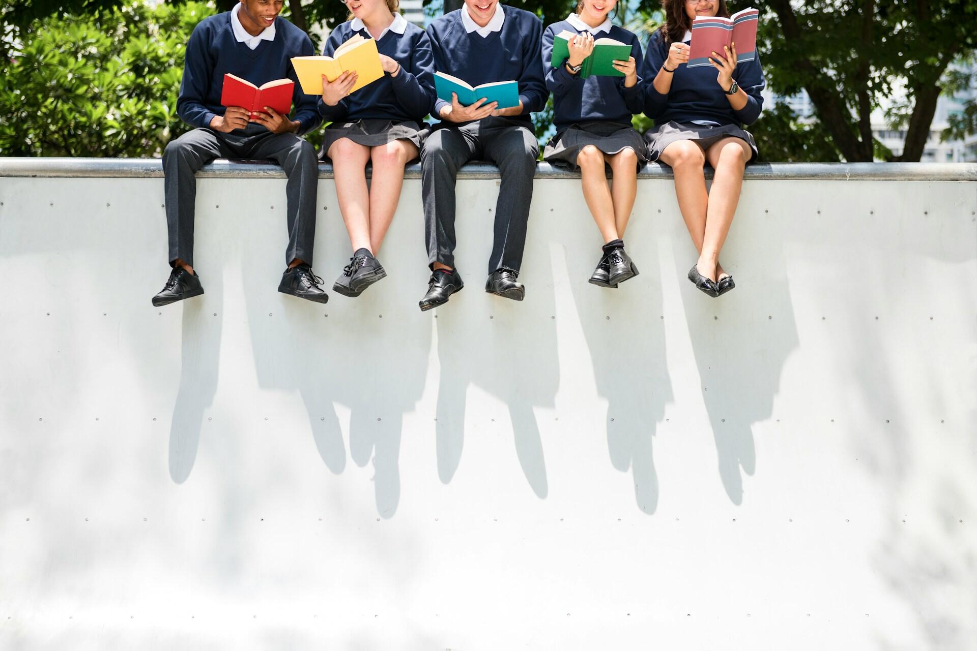 students sitting on a wall reading a book