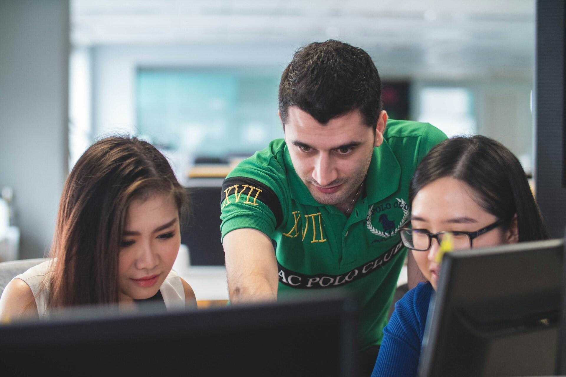 A teacher teaching two students at computers.