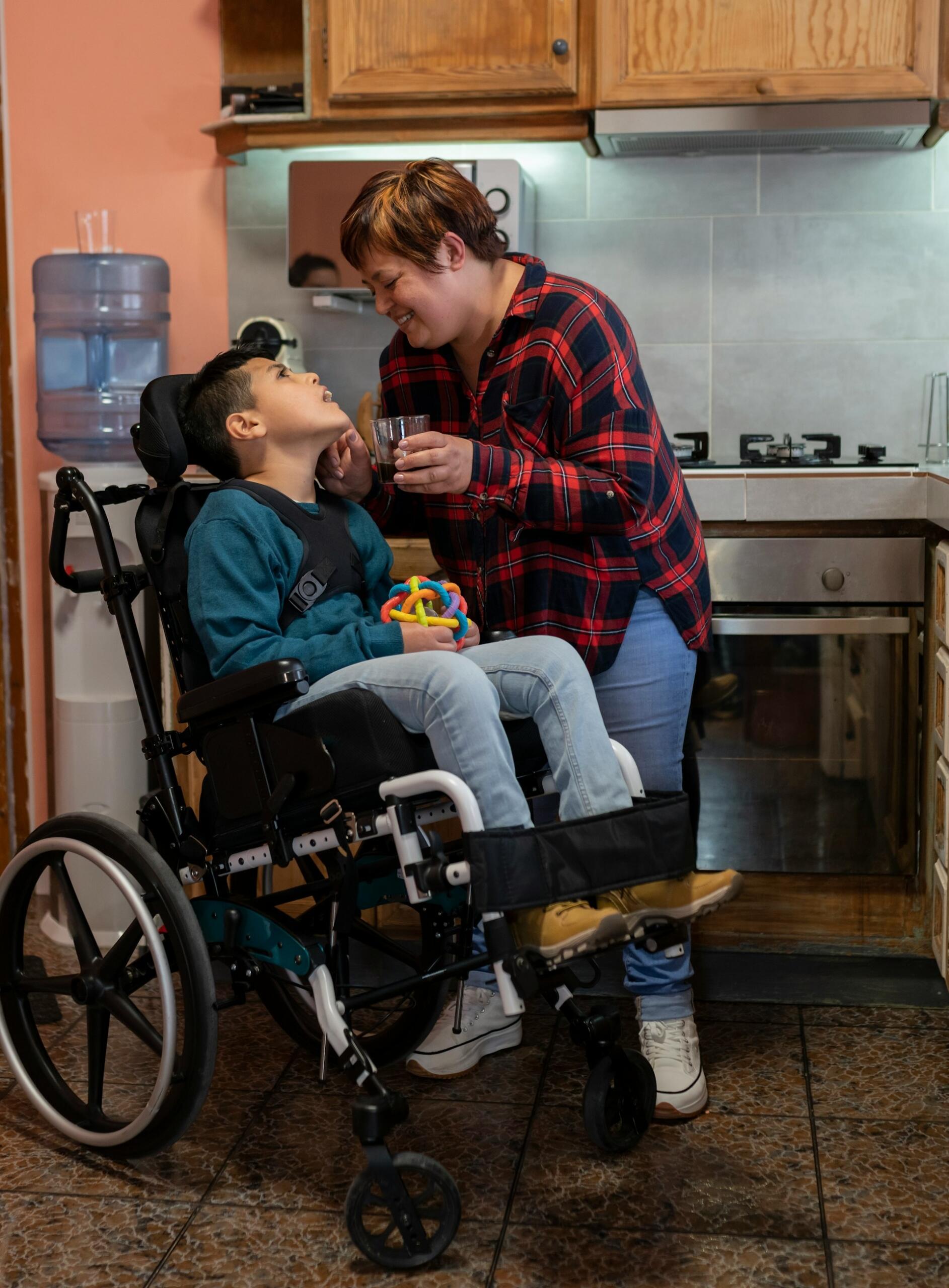 A child in a wheelchair with a woman giving a glass of water.