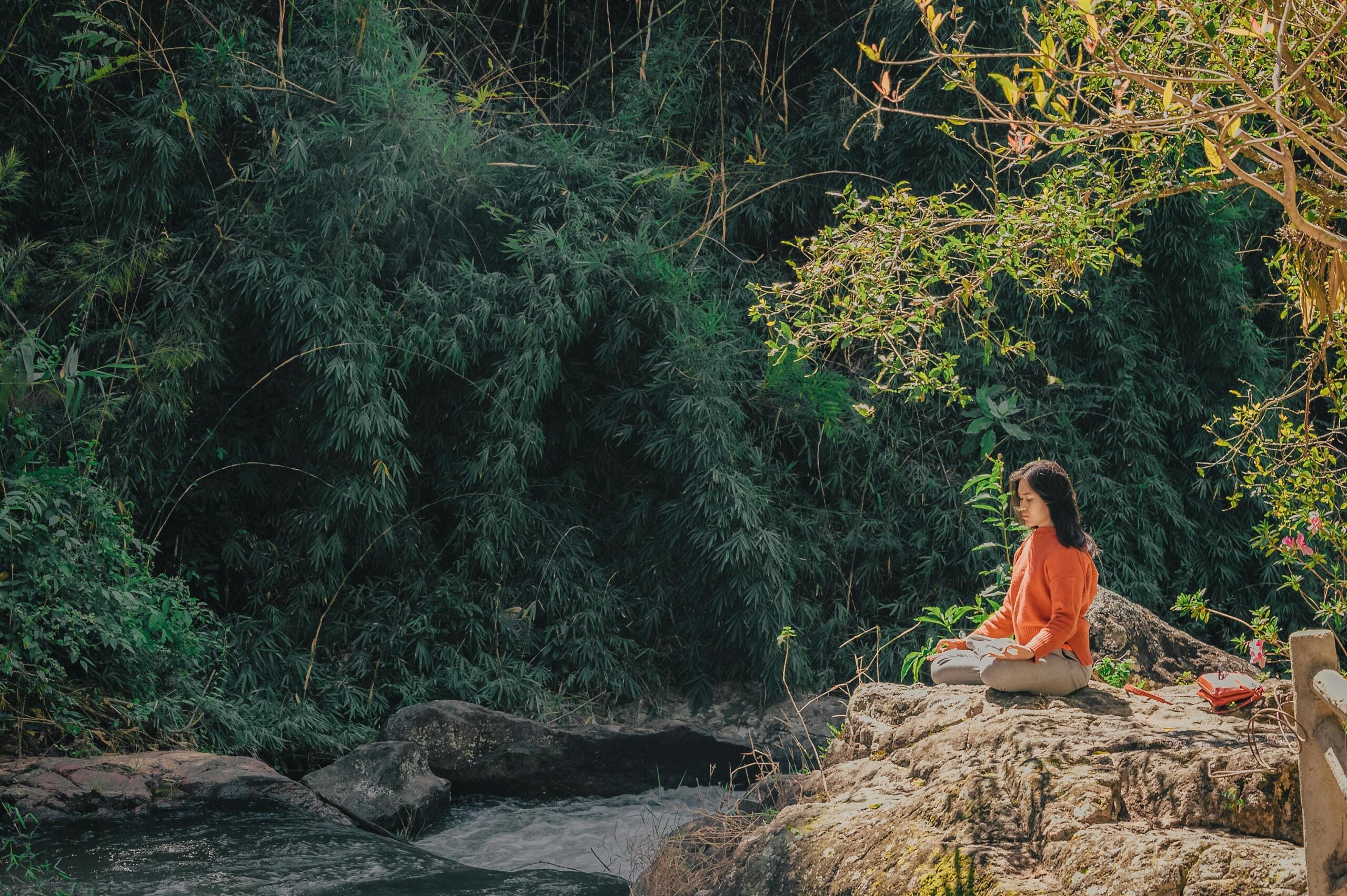 lady in orange clothing sitting next to a river 