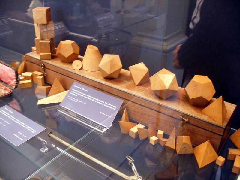A set of wooden geometric solids displayed neatly in a glass case, showcasing their shapes and smooth crafted surfaces.