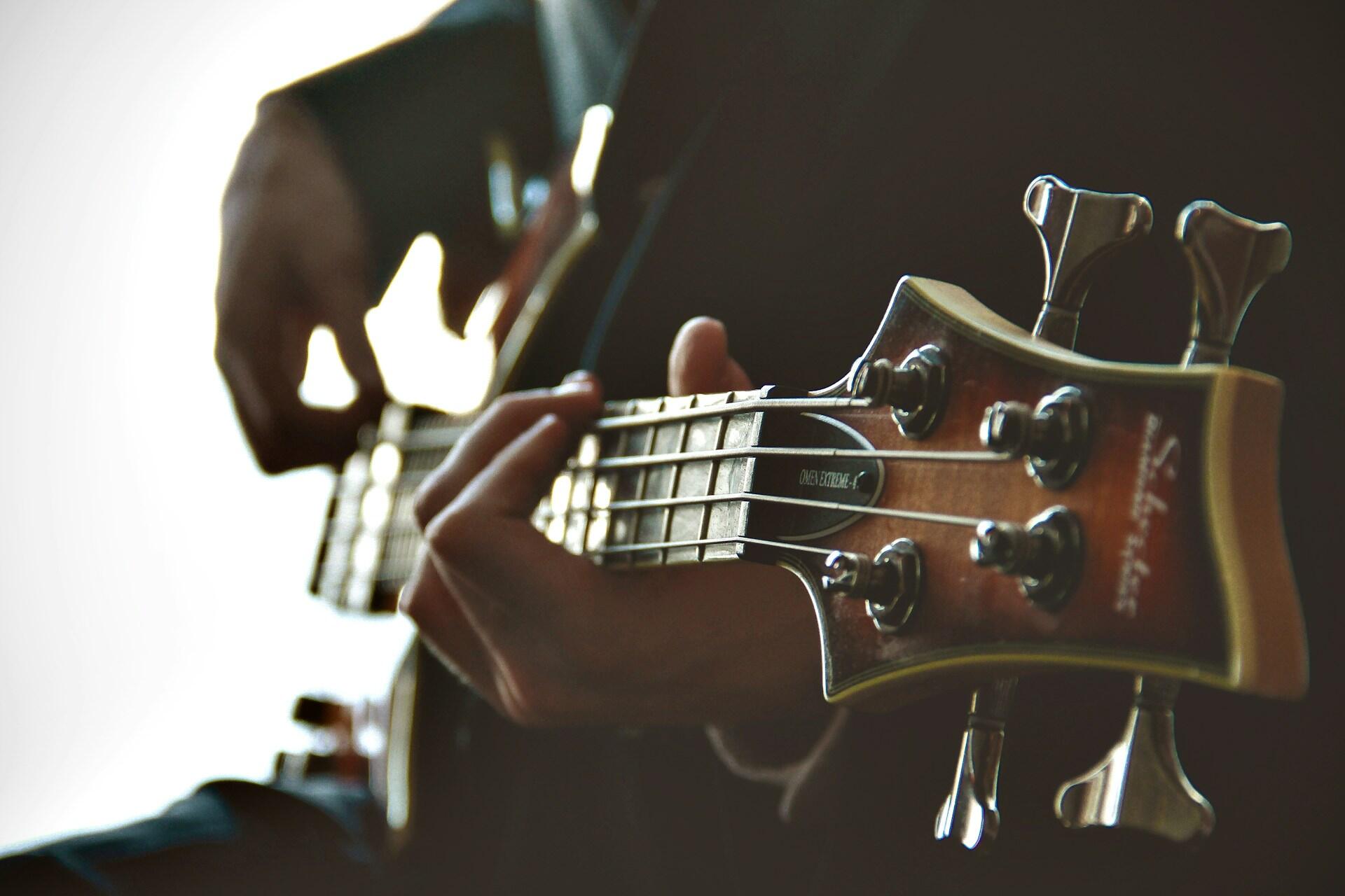 Hands playing a bass guitar with focus on the headstock and strings