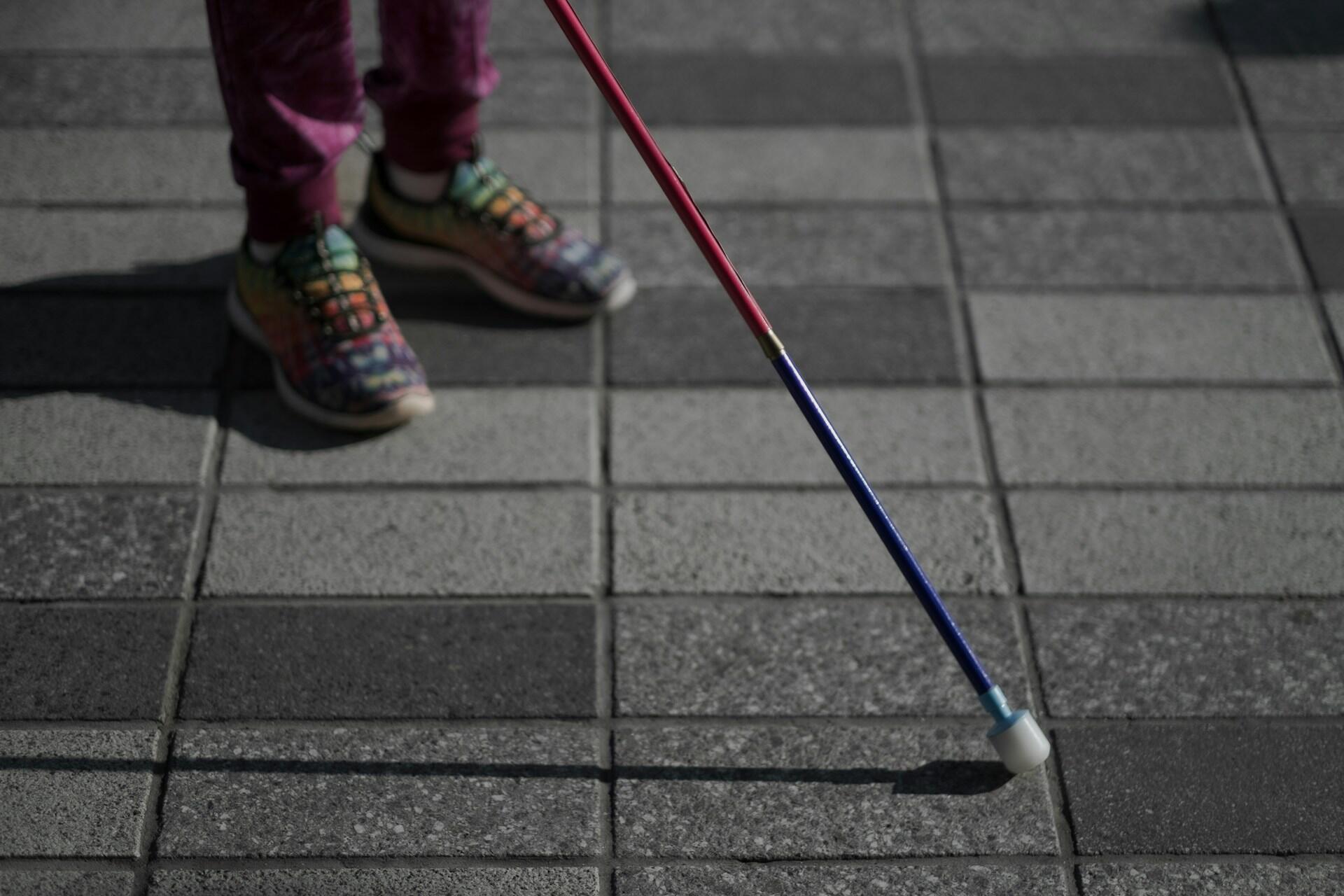 A child wearing colourful shoes on a sidewalk with a cane. 