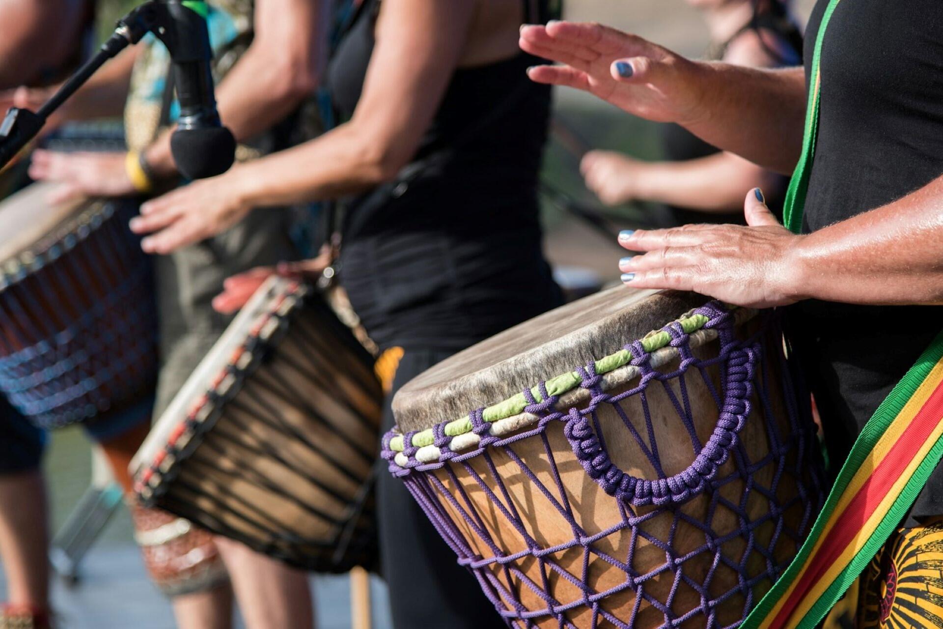 Group of people playing hand drums outdoors during a live percussion performance.