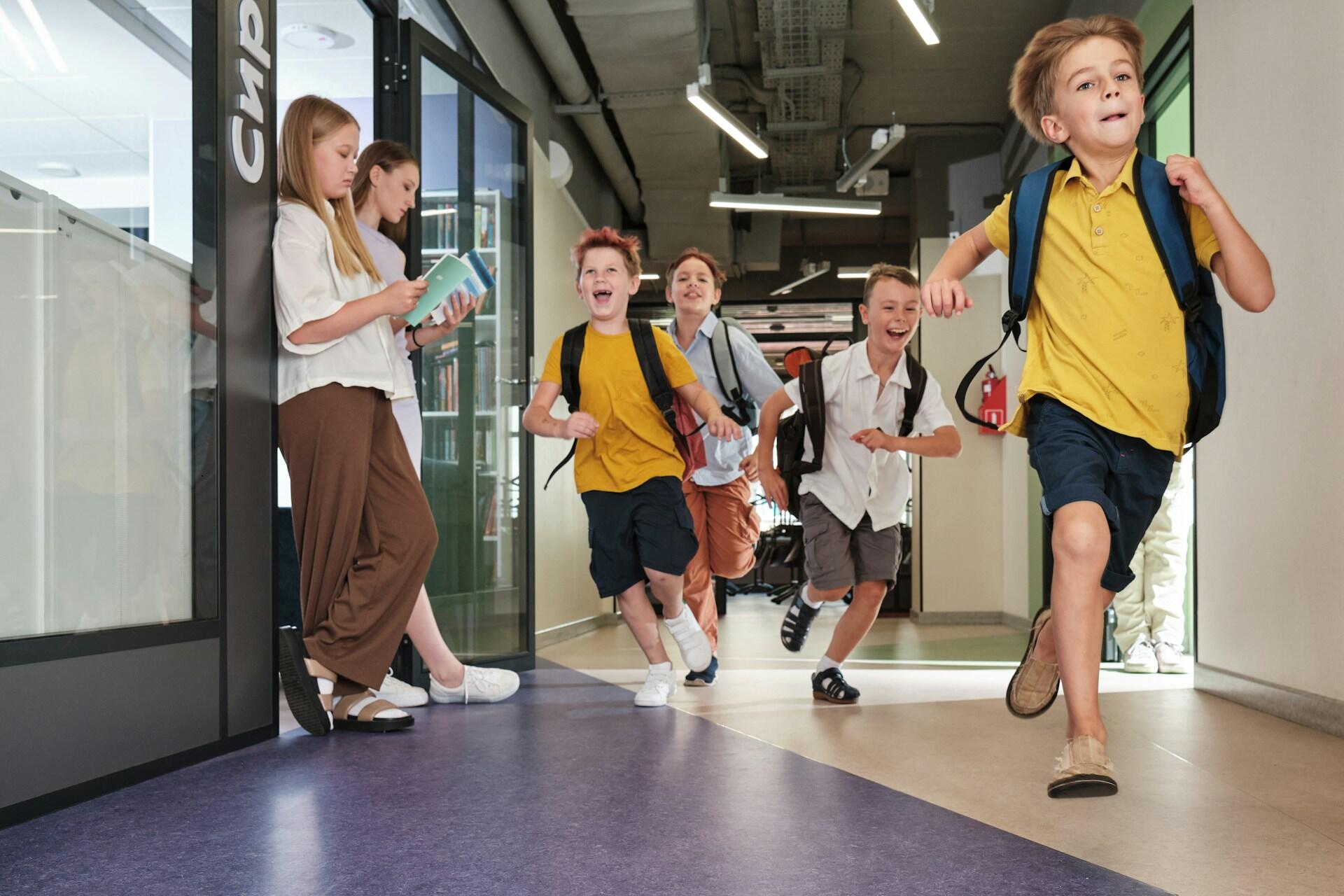 Children with backpacks running in a school hallway.