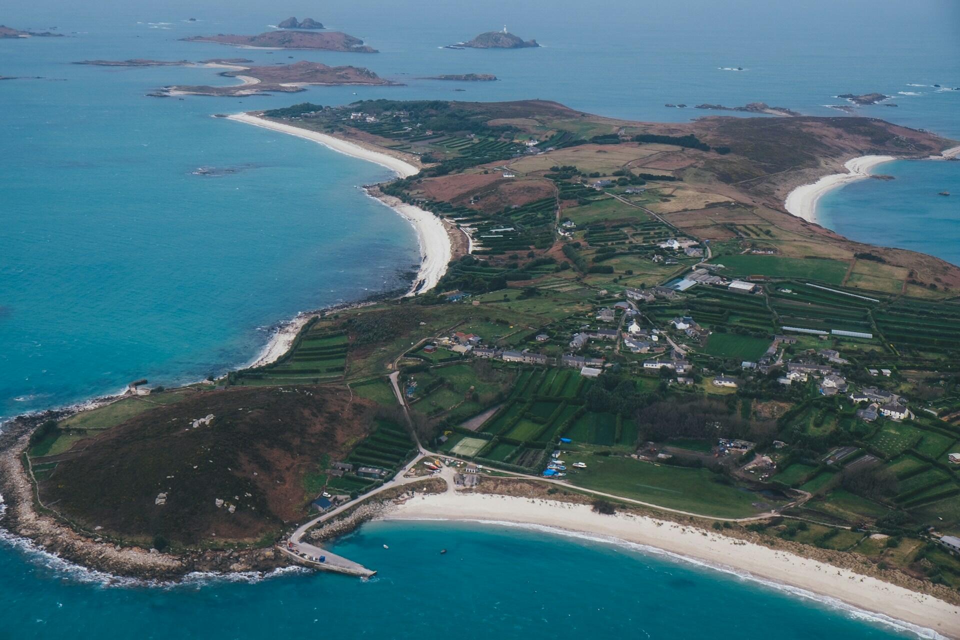 Aerial view of a coastal landscape featuring sandy beaches, green fields, and small villages, surrounded by blue waters and rocky islands.