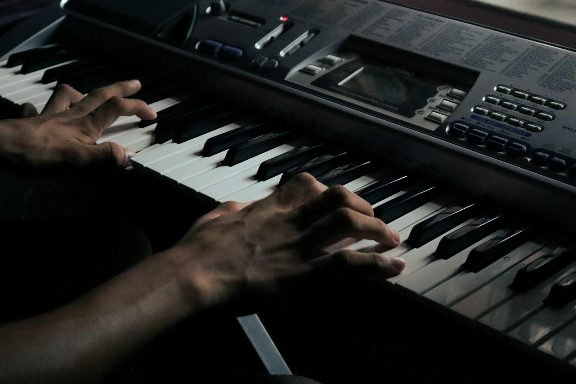 Hands playing notes on an electronic keyboard in low light.