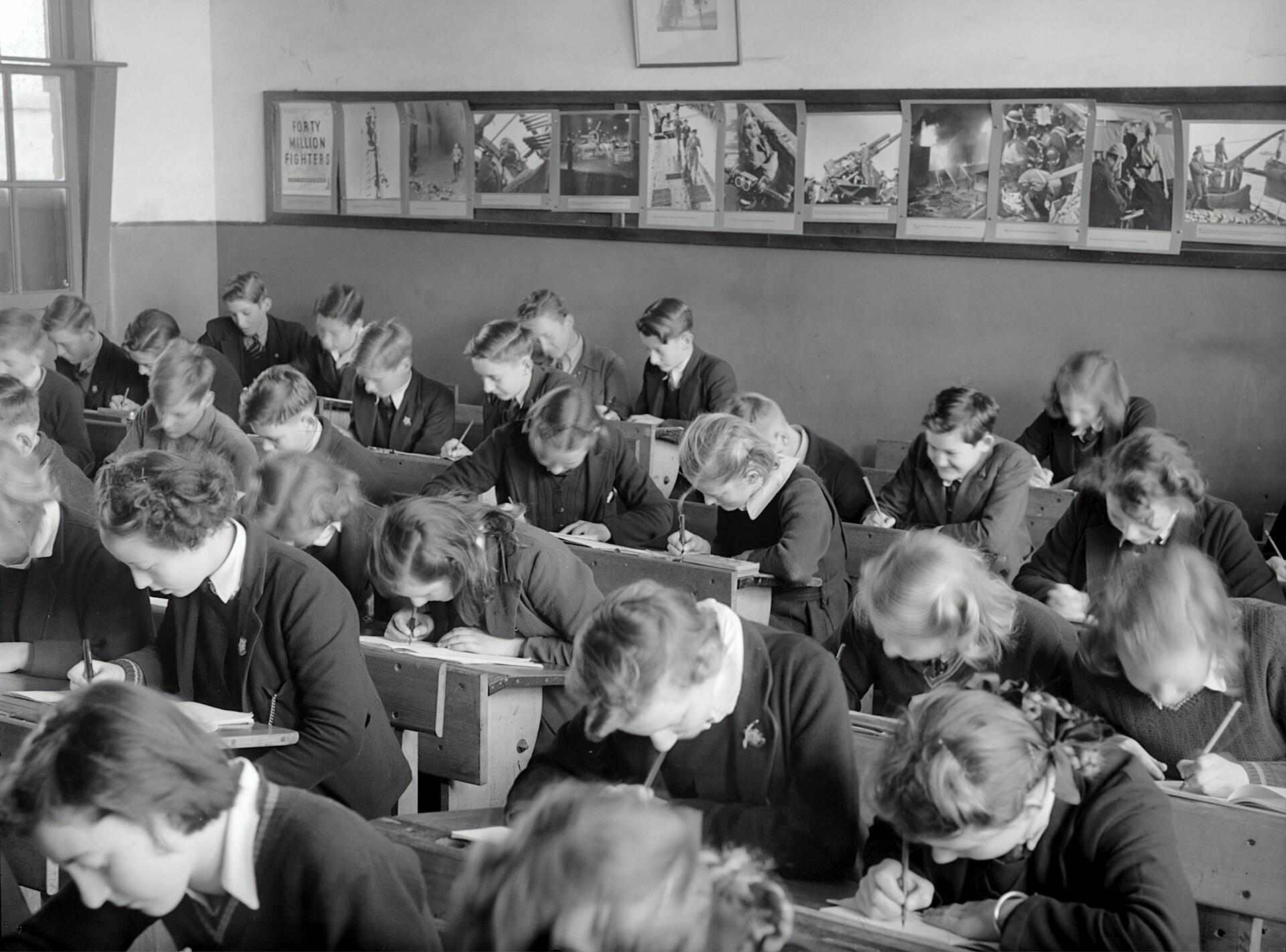 A classroom of students with their heads bent to their task of writing. 