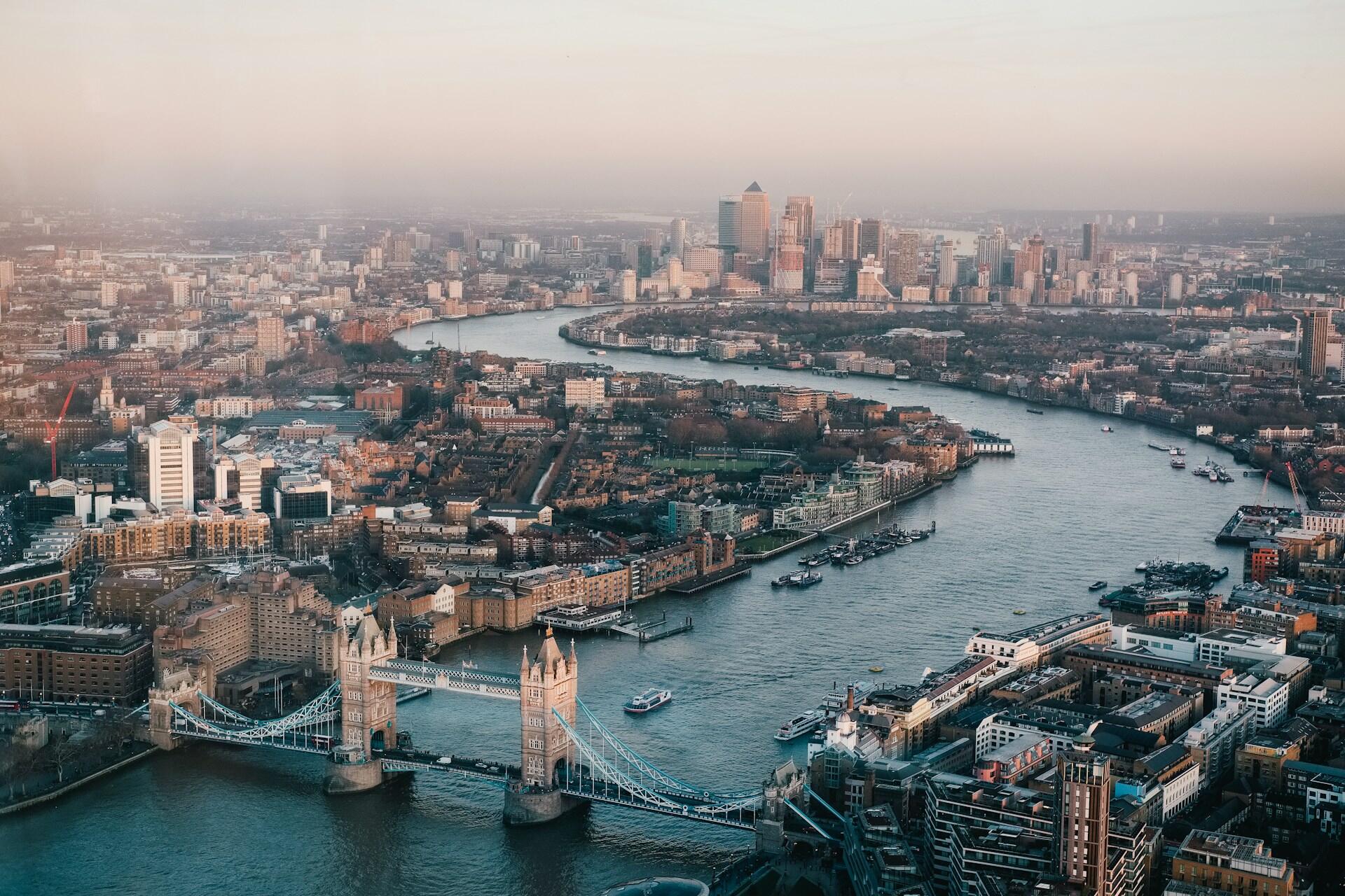 A panoramic view of London featuring the Tower Bridge, the Thames River, and a skyline of modern buildings in the background.