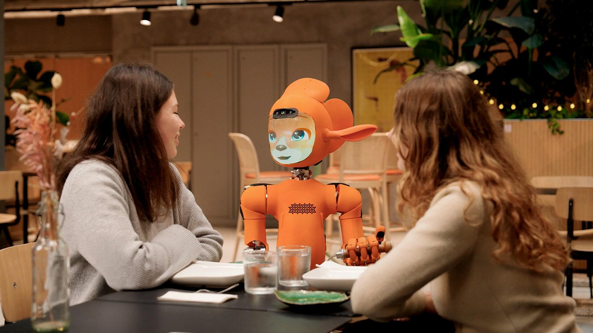 An orange humanoid robot taking a food order in a restaurant. 