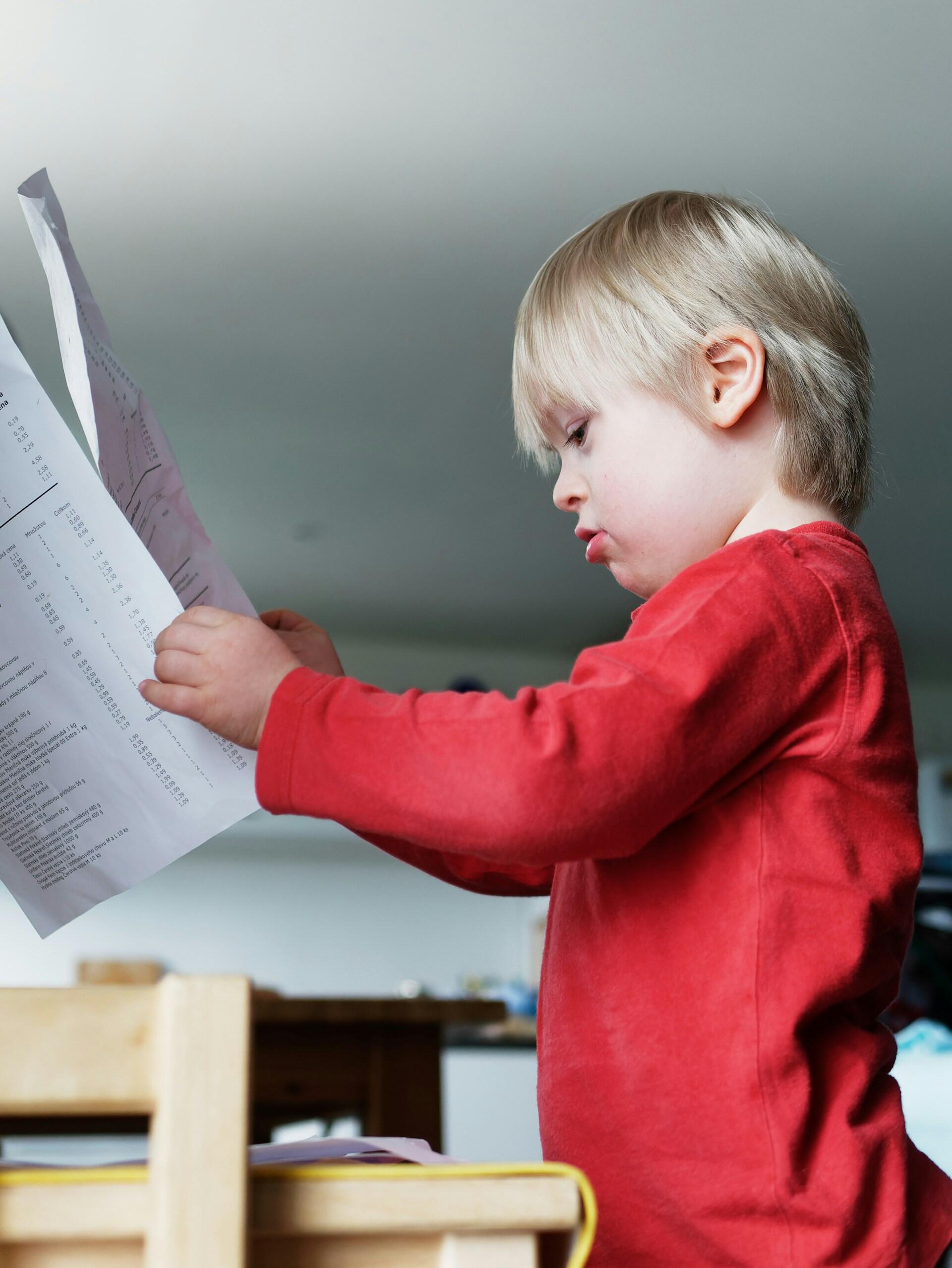 A blond child in a red jumper holds up papers as they scan them. 