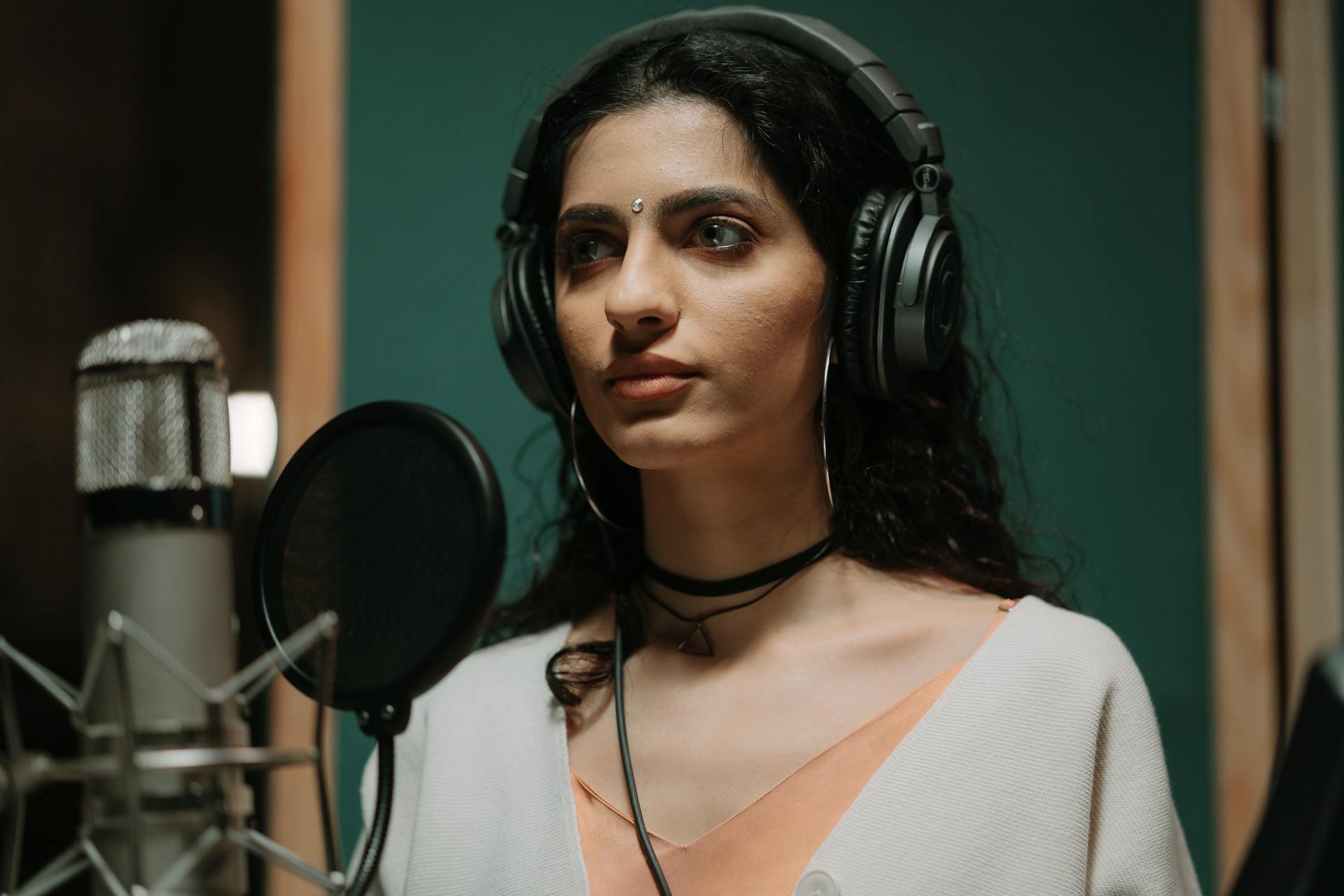 Lady singing into a mic while wearing headphones 