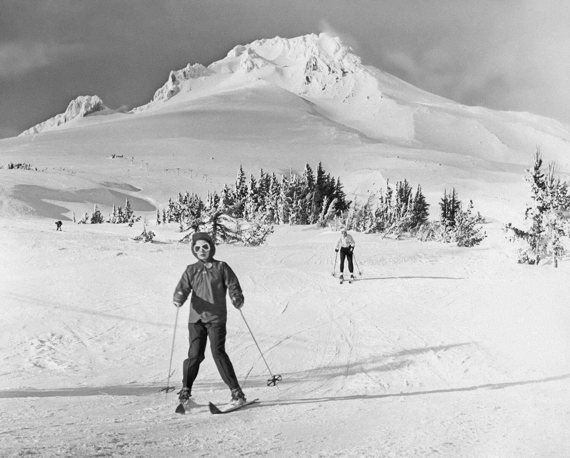 A black and white photo of a skier in front of the slopes.