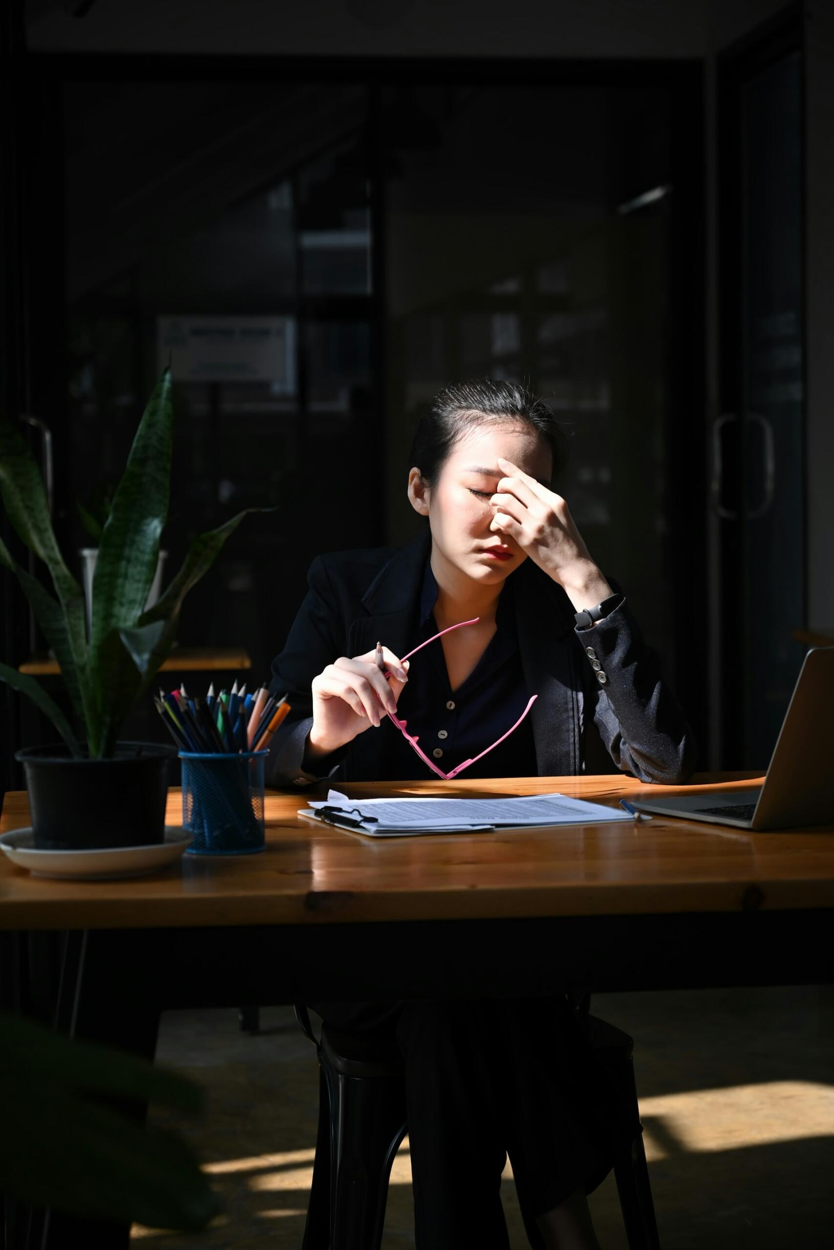 A woman at a desk squeezing her eyes with her hand in a stress expression. 